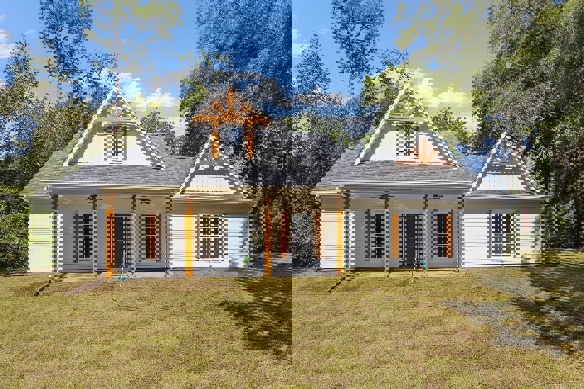 Two-story house with white siding, blue front door, and white-framed windows, surrounded by green lawn, mature trees, and a bicycle near the entrance; green tripod with white light