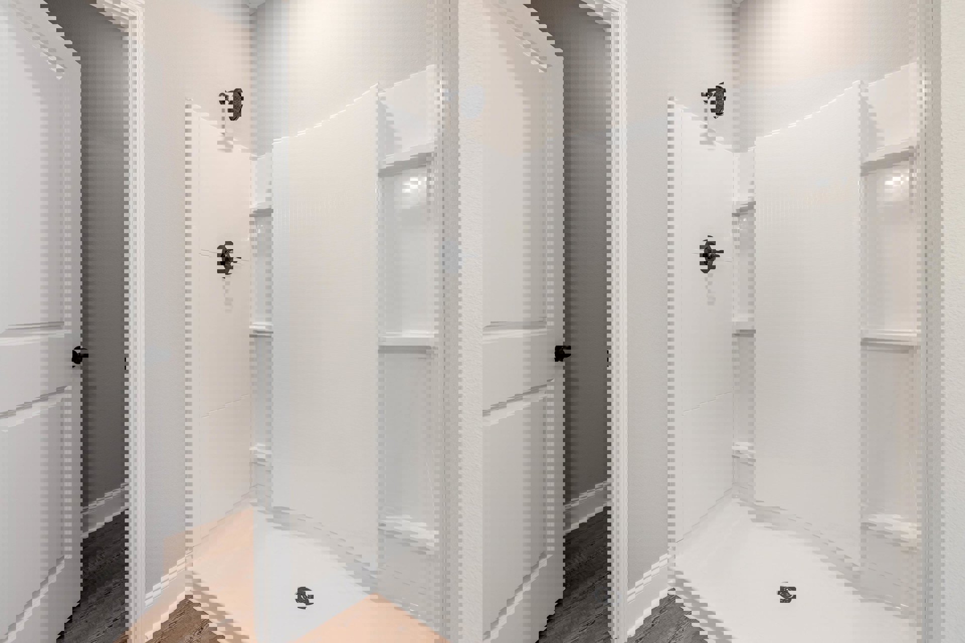 Walk-in shower with white tile walls, chrome shower head, linear drain, white door with black handle, and black light switch on plaster wall