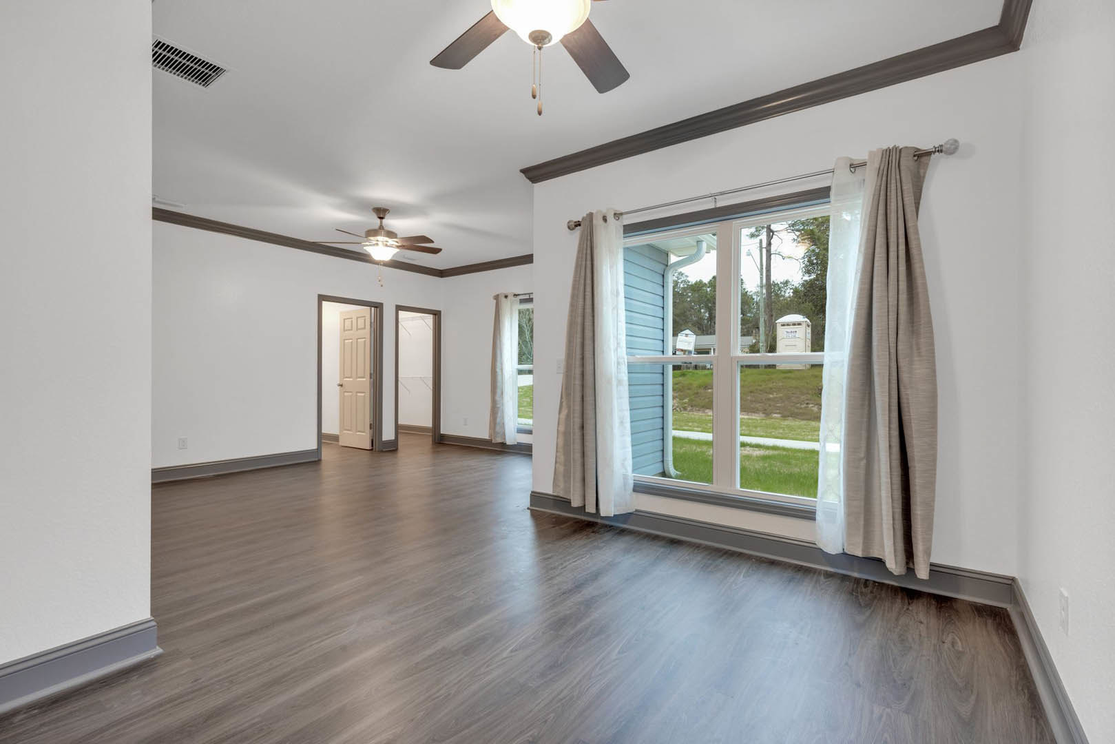 Hardwood flooring, white plaster walls, large window with sheer curtains, ceiling fan overhead