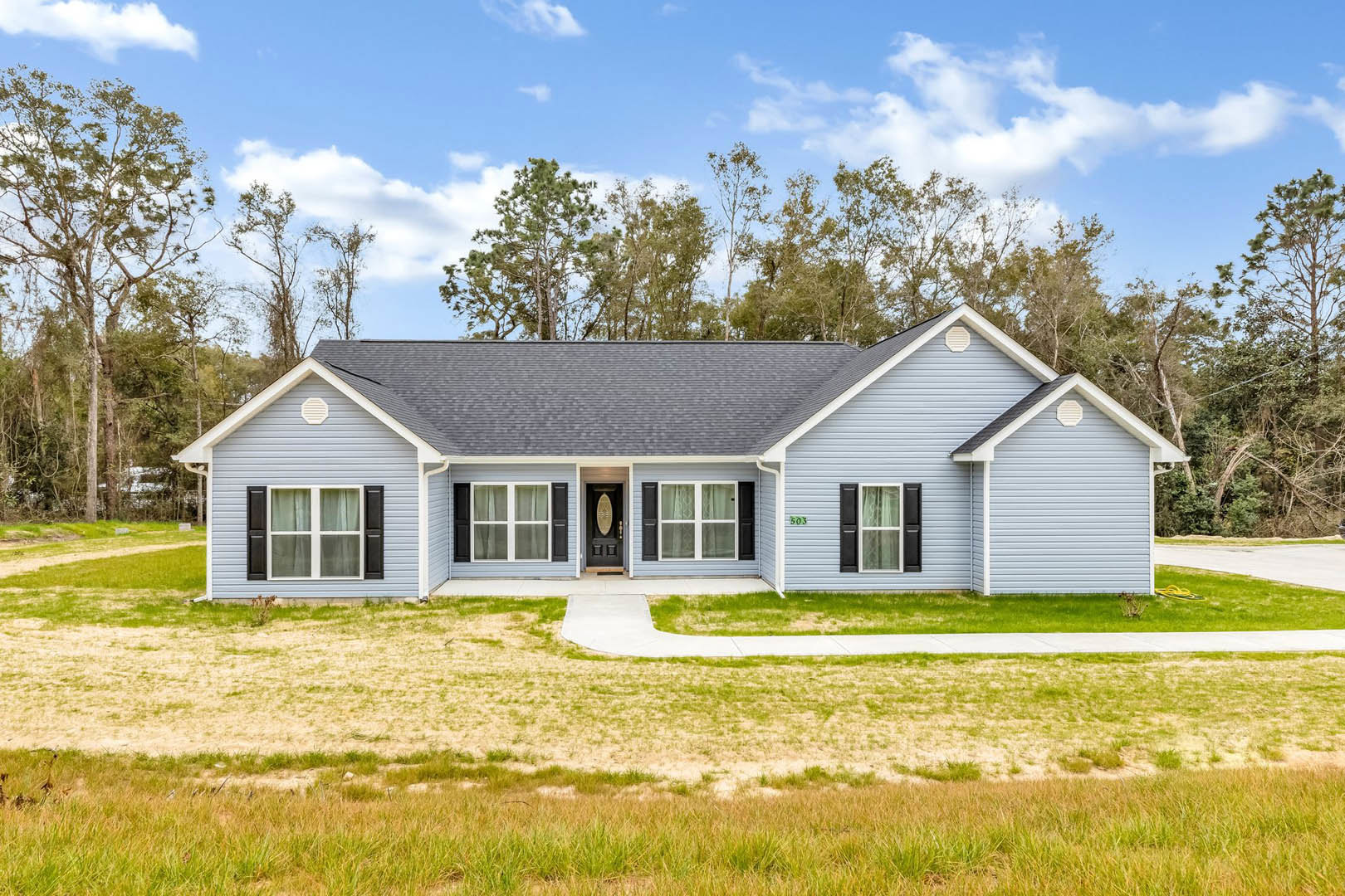 Two-story home with white siding, black shuttered windows, covered front porch, dark front door, manicured lawn, stone walkway, and mature trees in the background