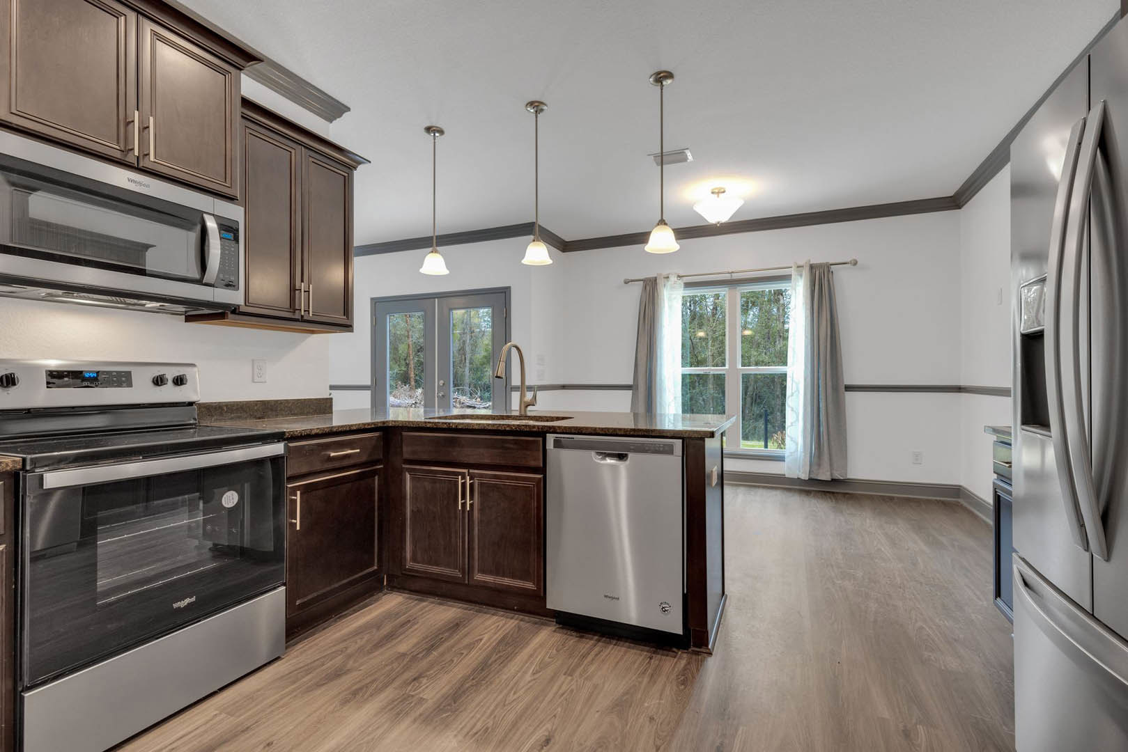 Open kitchen with wood flooring, stainless steel appliances including stove with glass door, dishwasher, refrigerator, and microwave, white cabinetry, large window overlooking