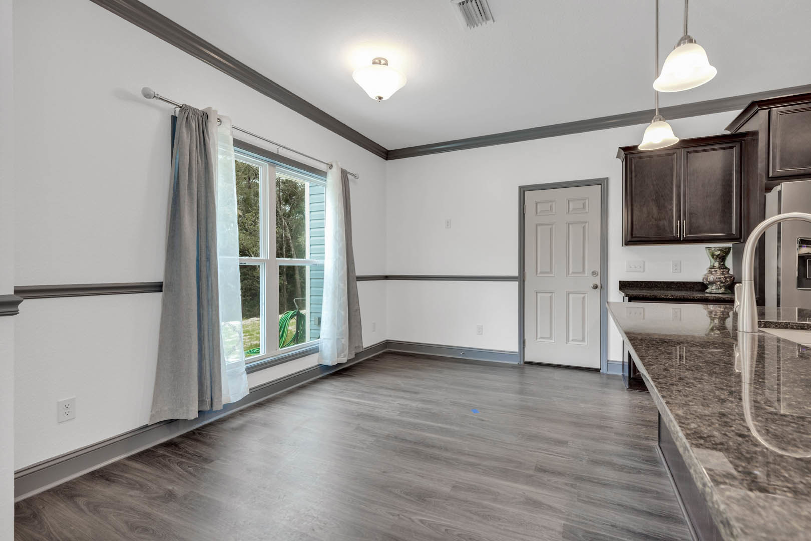 Marble countertop beneath a window, wood flooring, white door with silver handle, cabinetry, vase, and curtain
