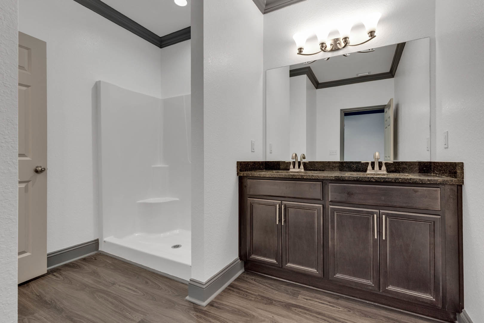 White tile shower with glass door, modern vanity with stone countertop and undermount sink, chrome faucet, light wood cabinetry, and neutral painted walls