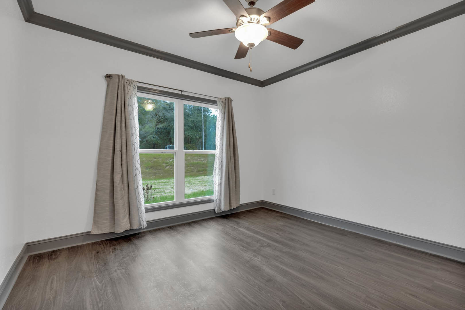 Wood floor room featuring a ceiling fan with light fixture, plaster walls, and a window dressed with curtains overlooking a grassy field.