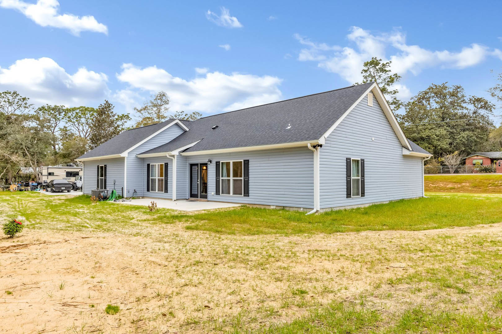 Two-story house with blue roof, white-framed windows, and grass backyard; small green plant with red bow near exterior, blue sky and clouds overhead