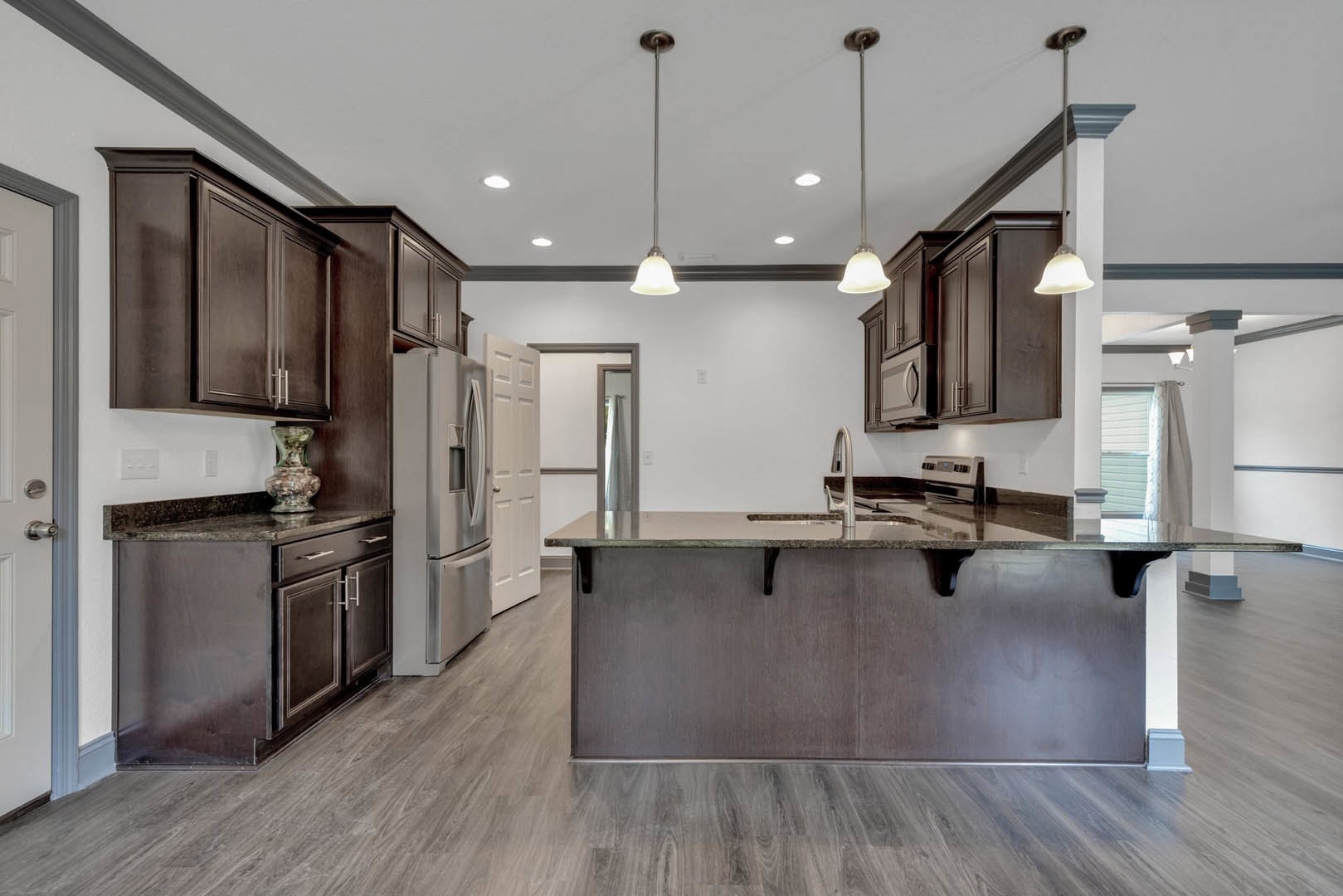 Kitchen with dark wood cabinets, central island with white countertop, stainless steel refrigerator, built-in sink, glass vase on island, light flooring, and recessed ceiling
