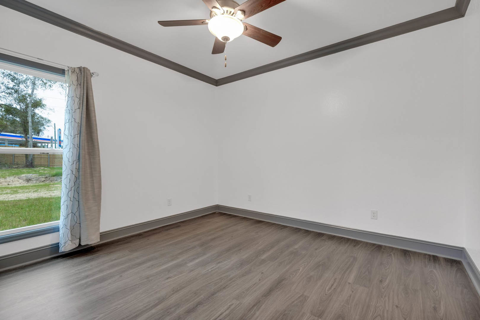 Ceiling fan with integrated light fixture above wood flooring, white plaster walls, and sheer curtain in a modern residential room