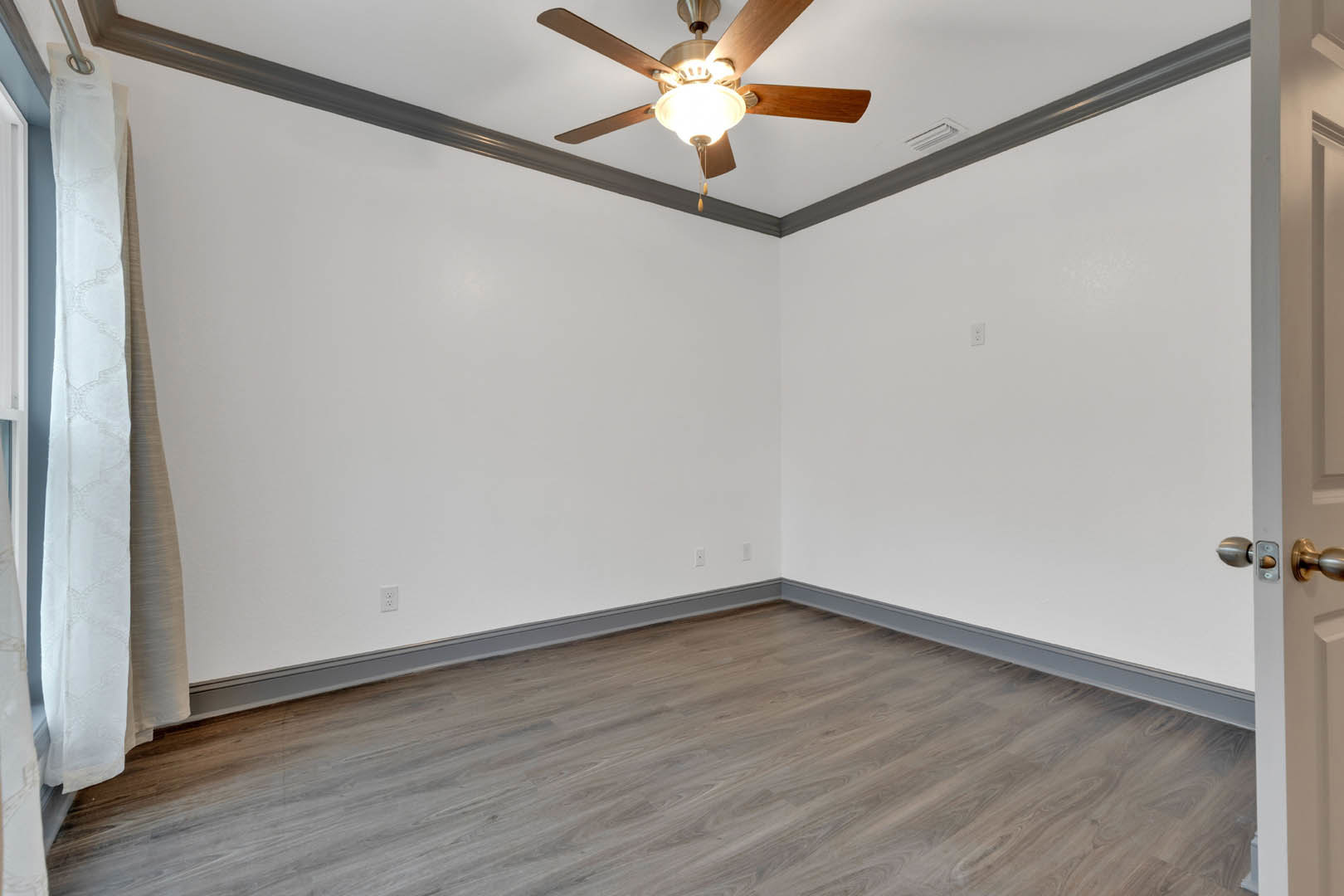 Ceiling fan with light fixture above hardwood floors, white plaster walls with base molding, close-up of brushed metal door knob, white towel hanging on door swing arm