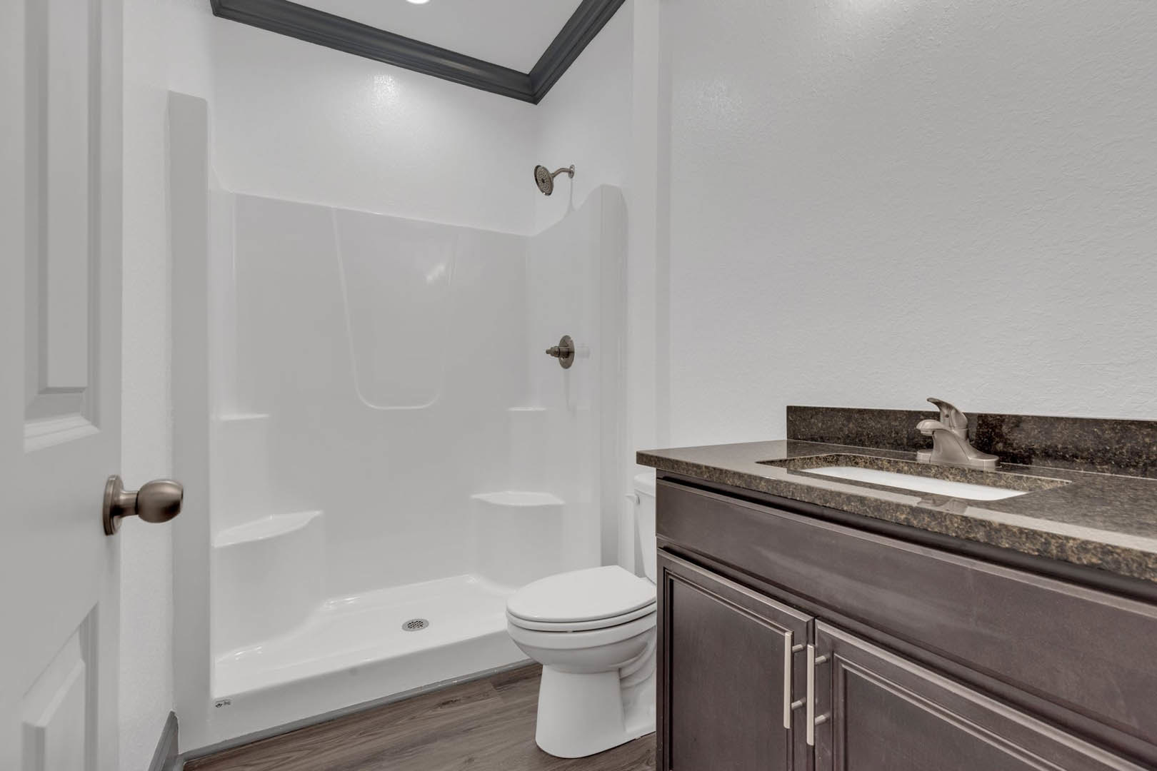 White porcelain sink and toilet with chrome faucet, light gray tile flooring, wall-mounted shower head, white painted ceiling, brushed metal doorknob, and modern cabinetry.