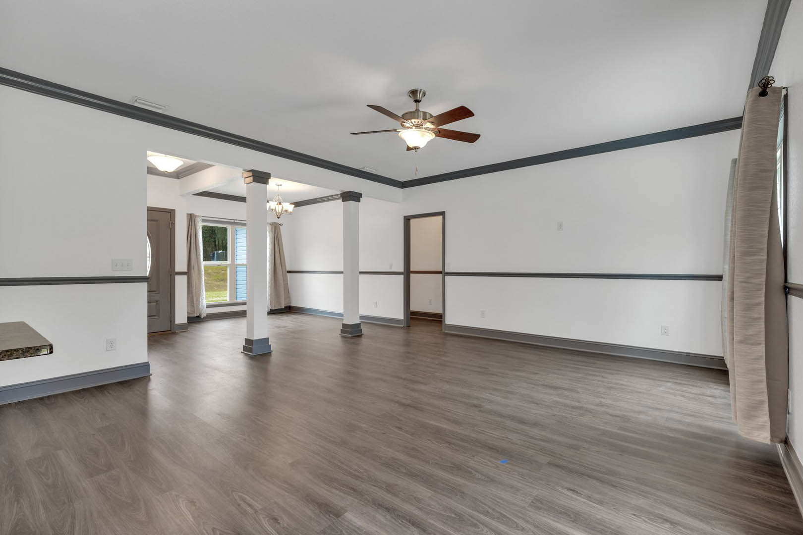 Spacious room with white plaster walls, wood laminate flooring, ceiling fan with light, and sheer curtains