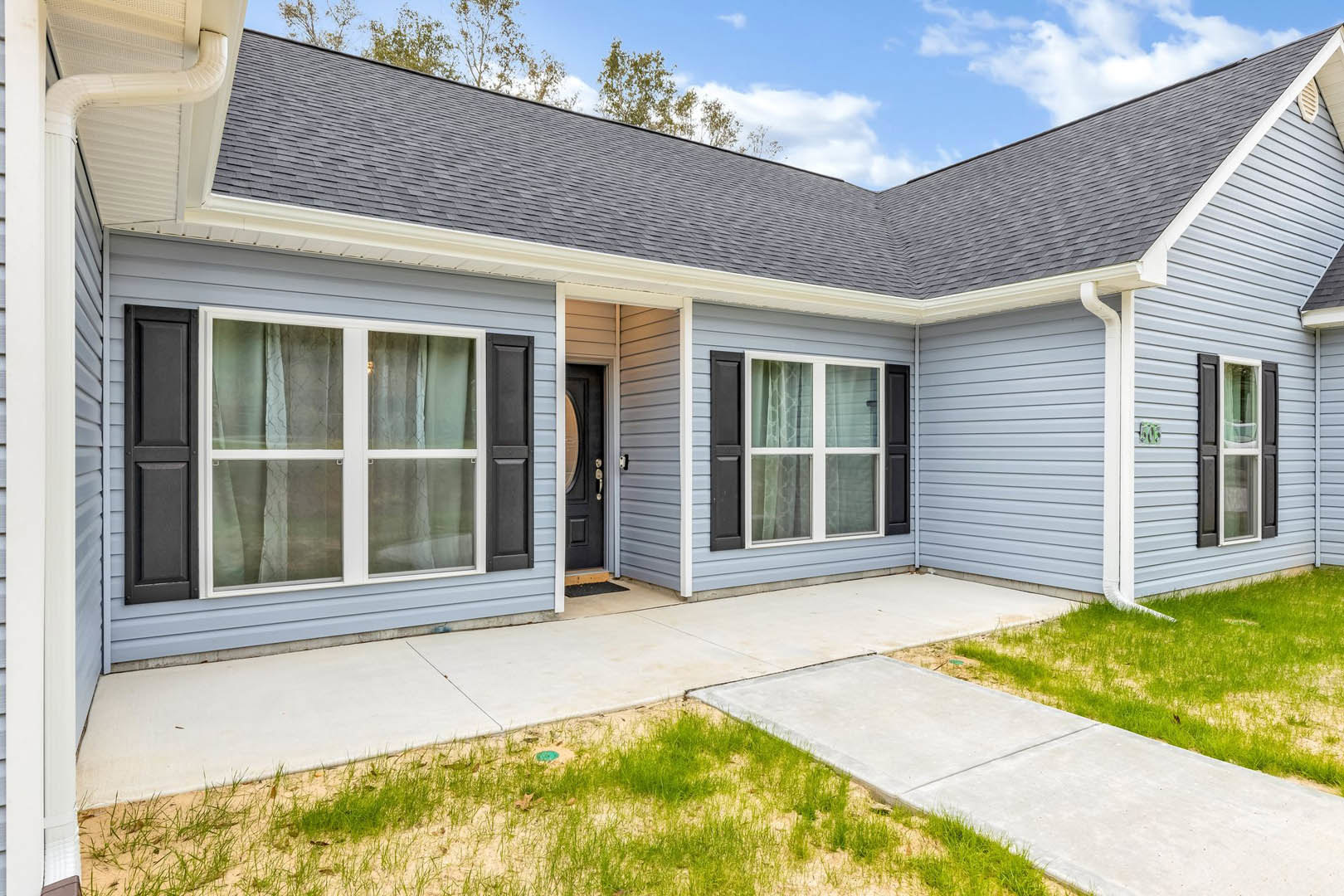 Two-story home with white siding, black shutters, and black front door; manicured green lawn and grass patch; windows with white frames and curtains; covered porch under partly