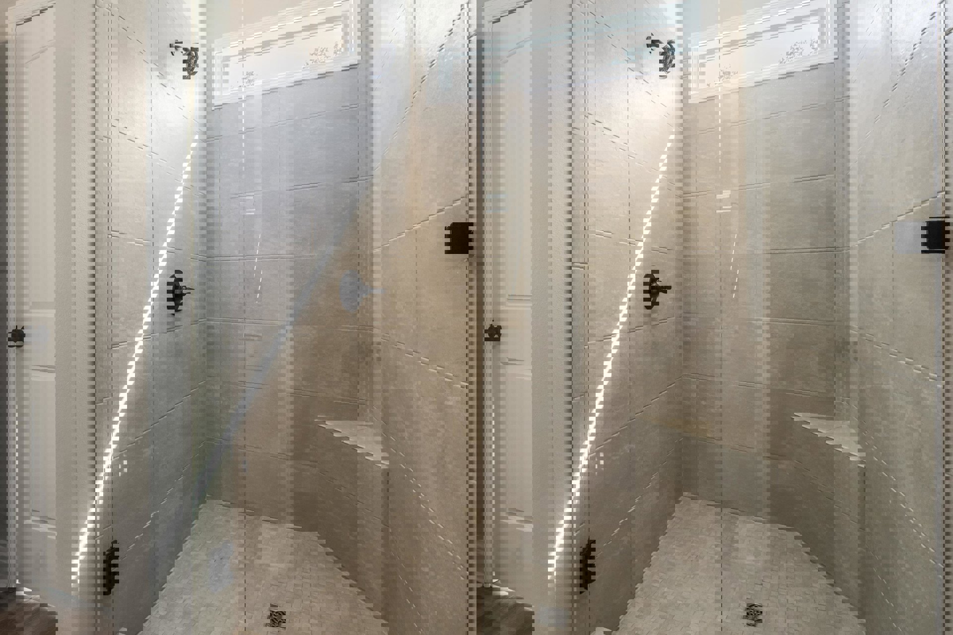 Marble tile shower with glass door, window letting in natural light, black wall-mounted fixture, and black switch on tile wall