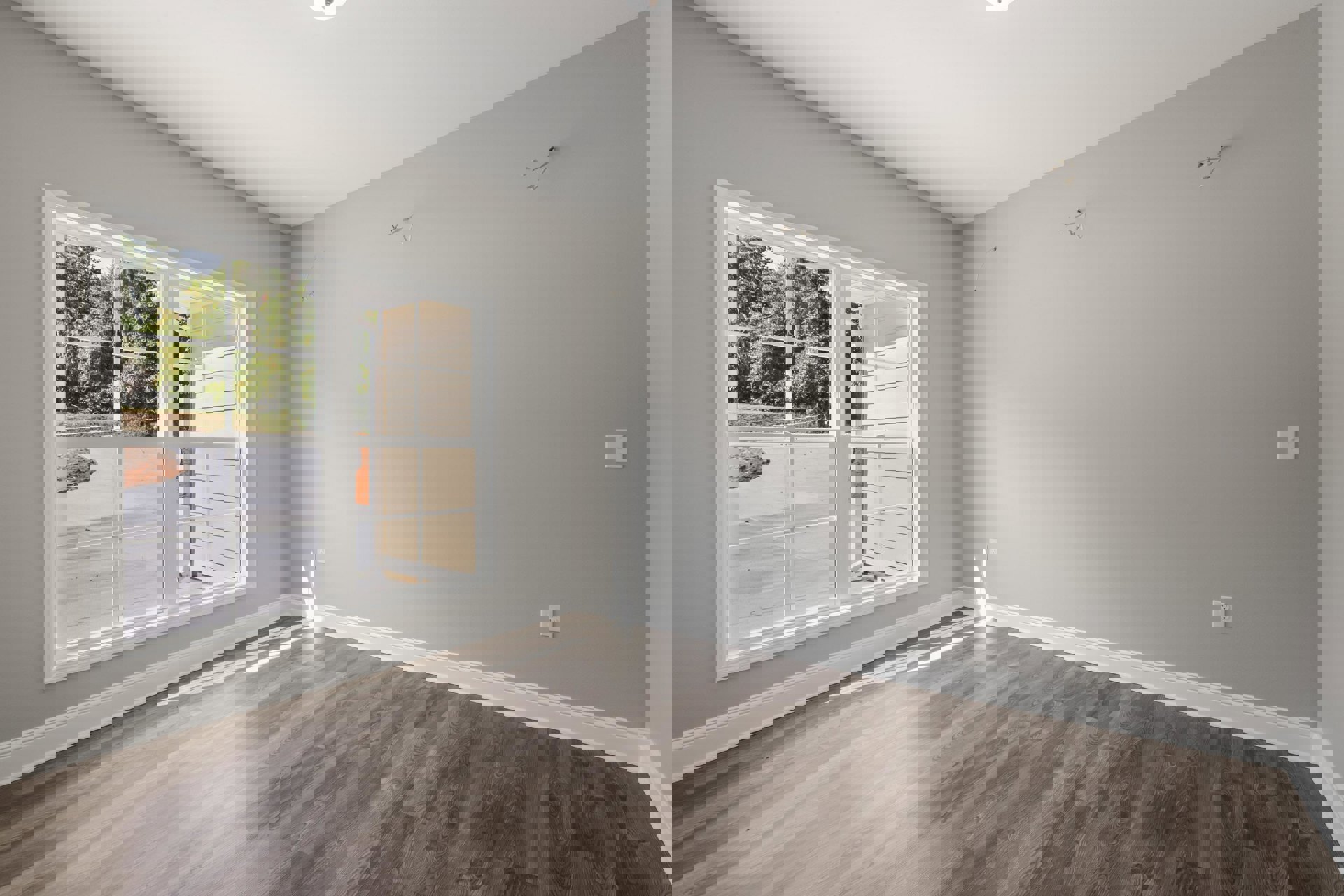 Wood flooring in a bright room with white plaster walls, large window overlooking a house and trees, visible white wire and black outlet on the wall