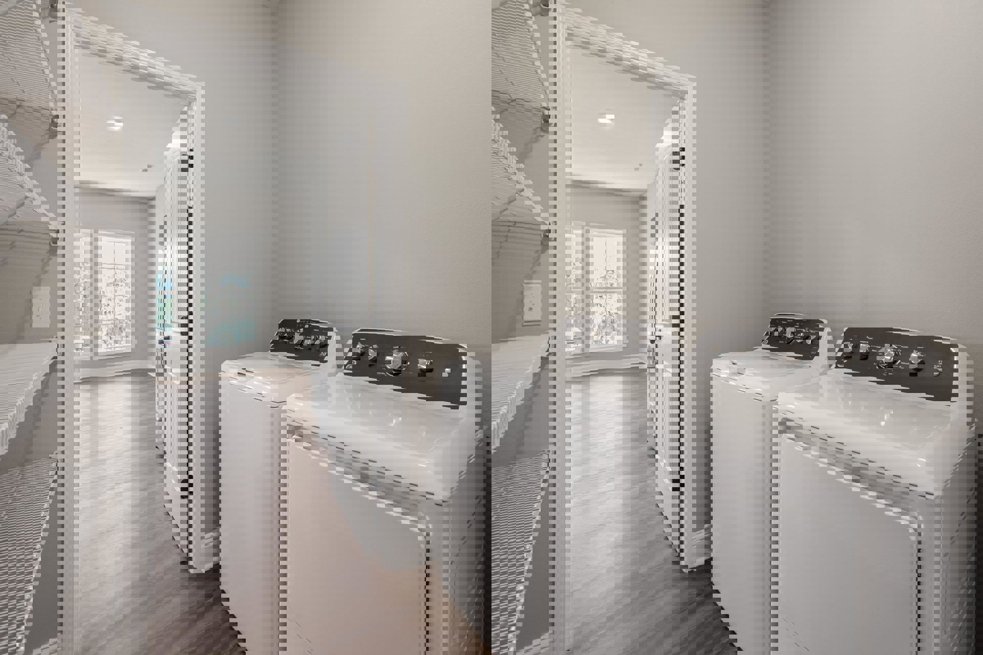 Laundry room with wood flooring, front-loading washer and dryer side by side, white-framed window, white cabinetry, visible drawer and knob, light switch on wall.