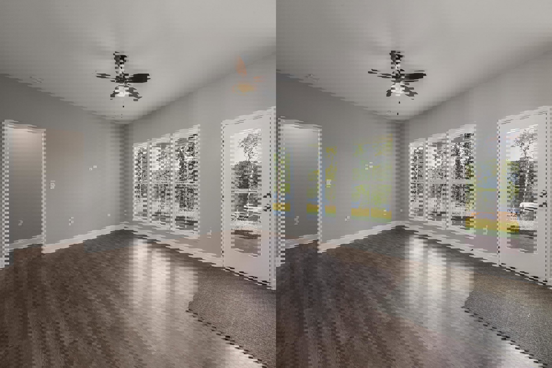 Ceiling fan with light fixture above wood flooring, large windows and glass door overlooking tree and lake, white wall frame, neutral area rug