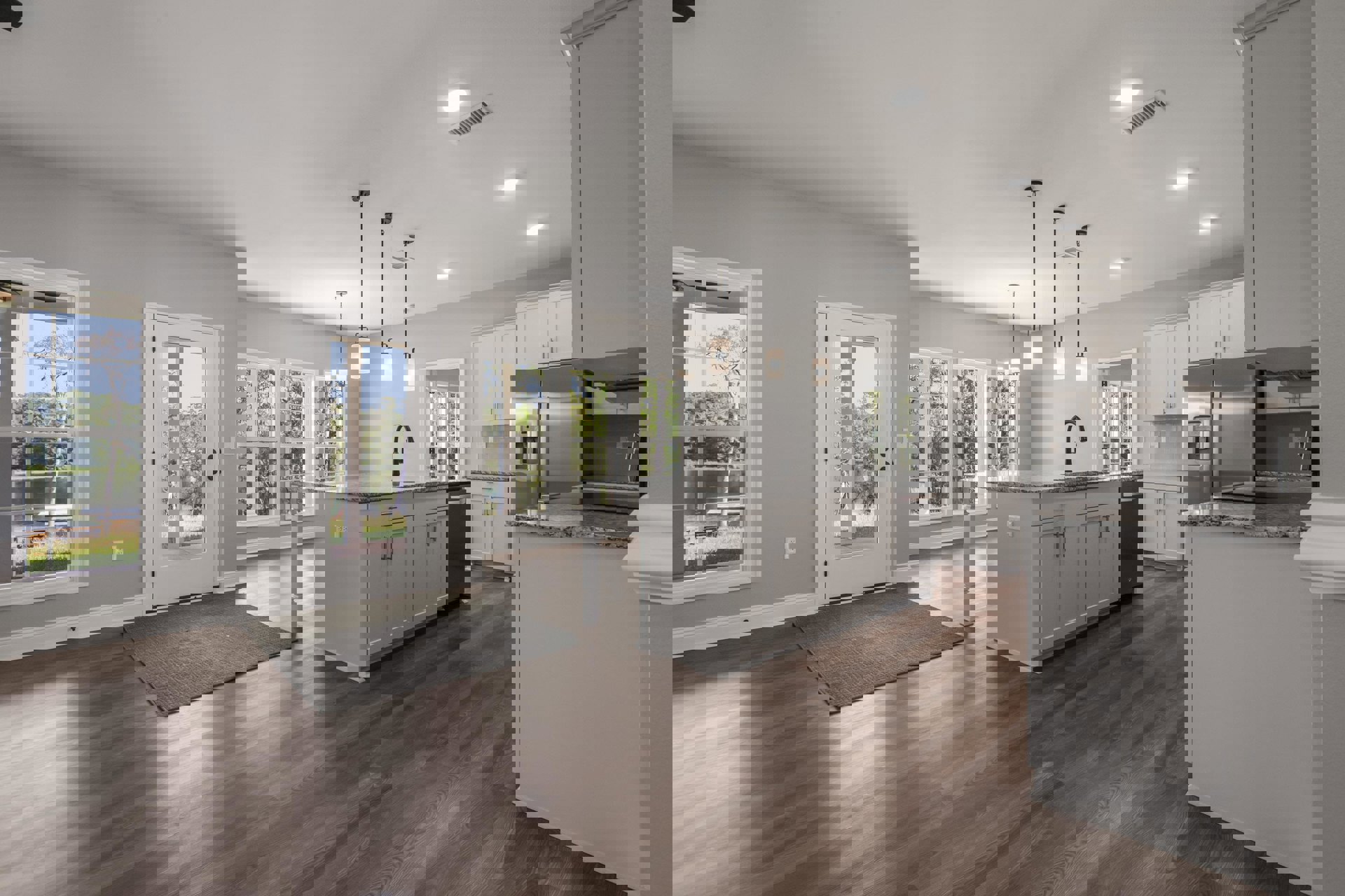 Open kitchen and dining area featuring hardwood floors, white cabinetry, black faucet on white countertop, large window and glass door offering views of lake and trees, grey carpet