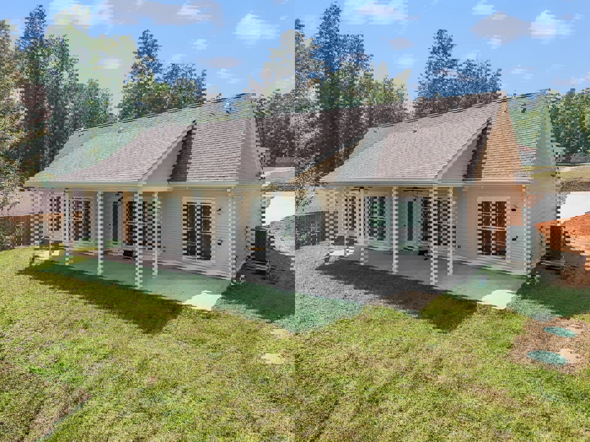 Two-story house with white siding, covered front porch, large windows, manicured lawn, mature trees in the background, and cloudy sky overhead