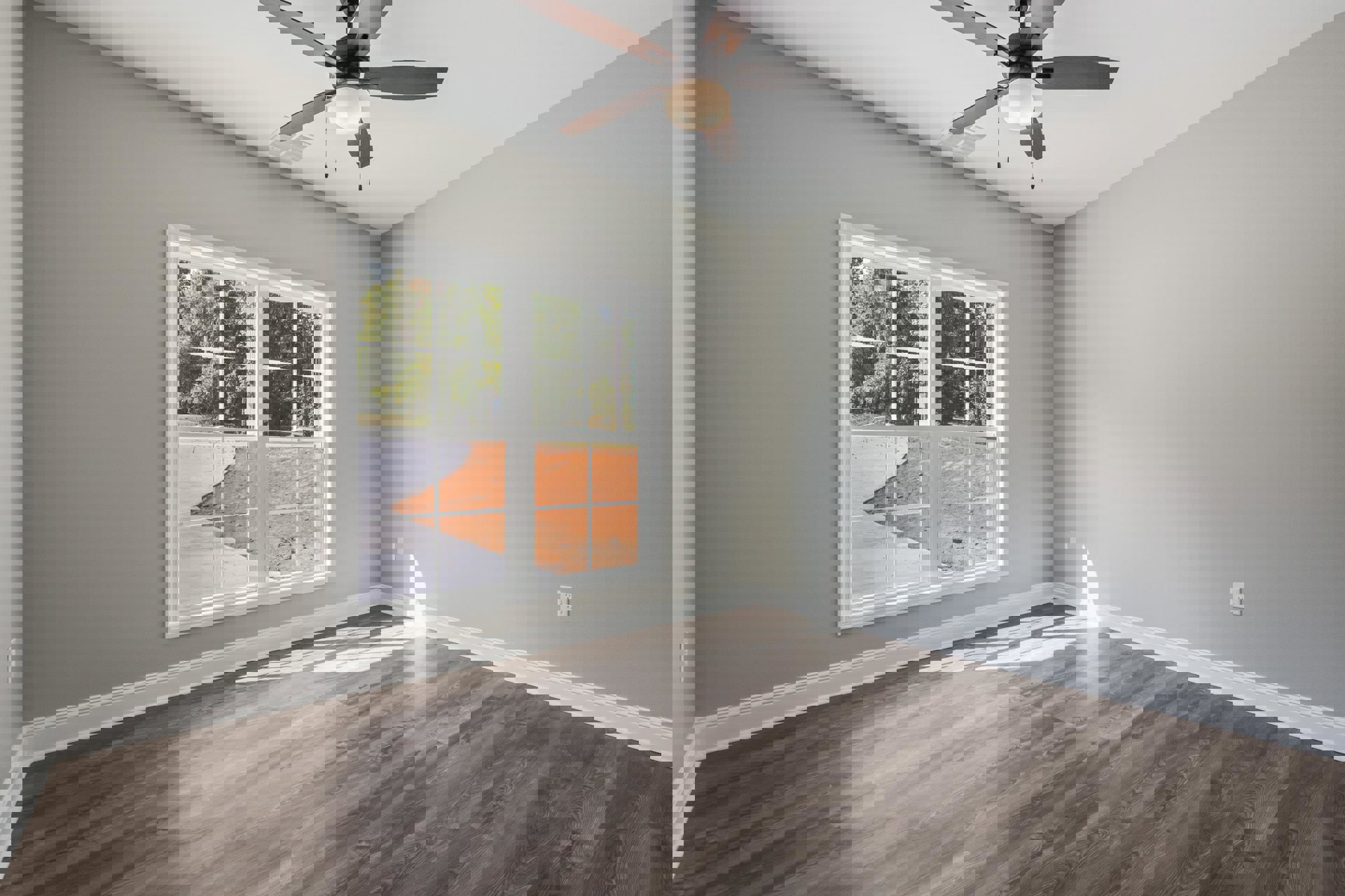 Wood flooring, white plaster walls, ceiling fan with integrated light, large window overlooking dirt path and trees