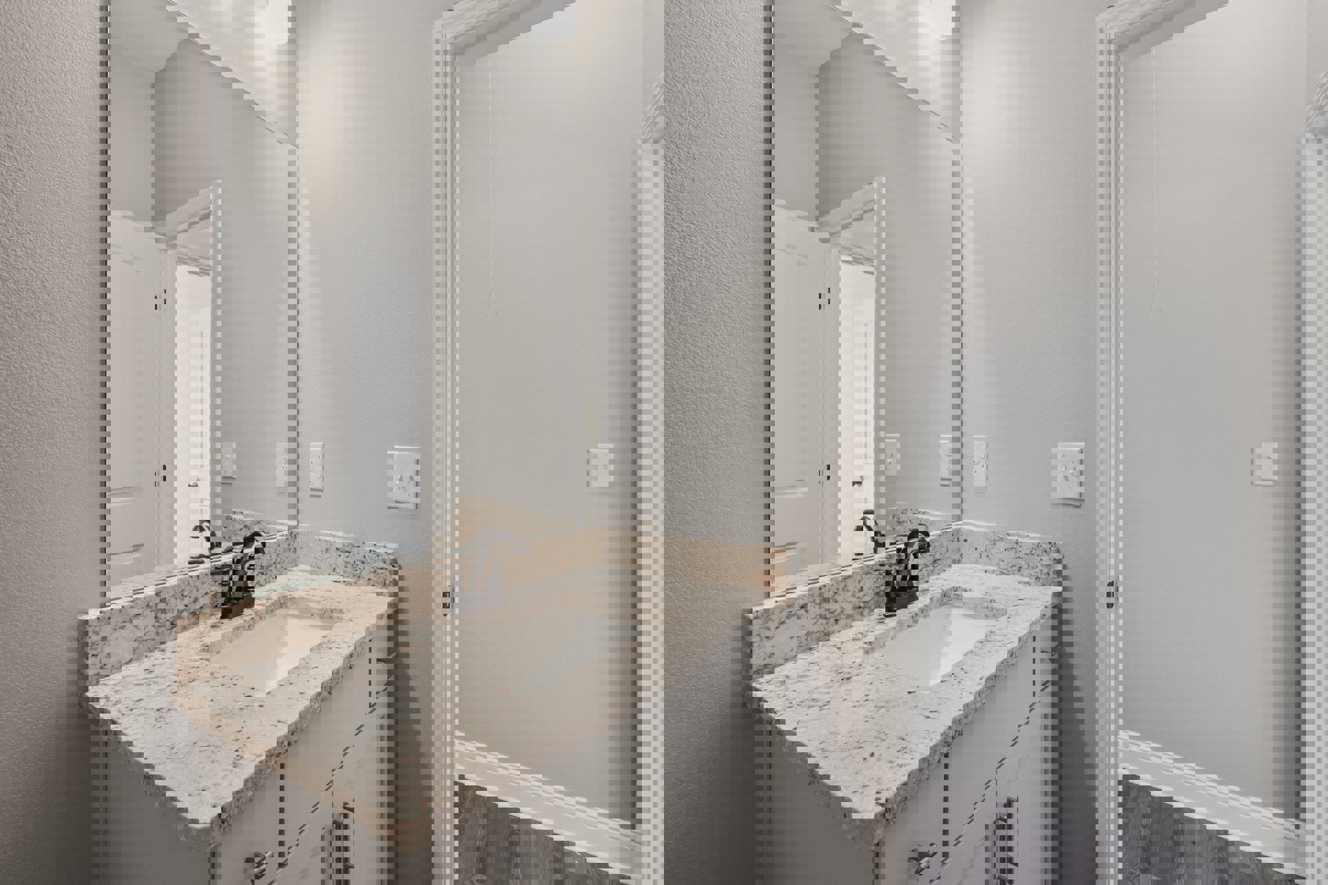 Marble countertop with undermount sink, chrome faucet, large framed mirror above, white cabinetry, tiled backsplash, and a double light switch on the adjacent wall.