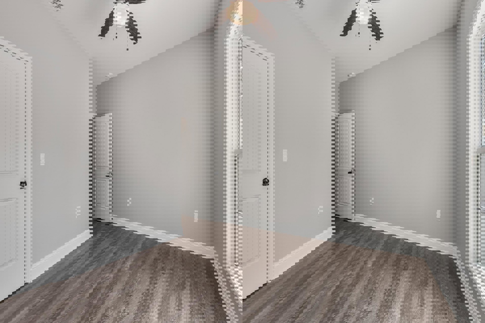 Ceiling fan with light fixture above wood laminate flooring, white door with black knob, plaster walls and molding