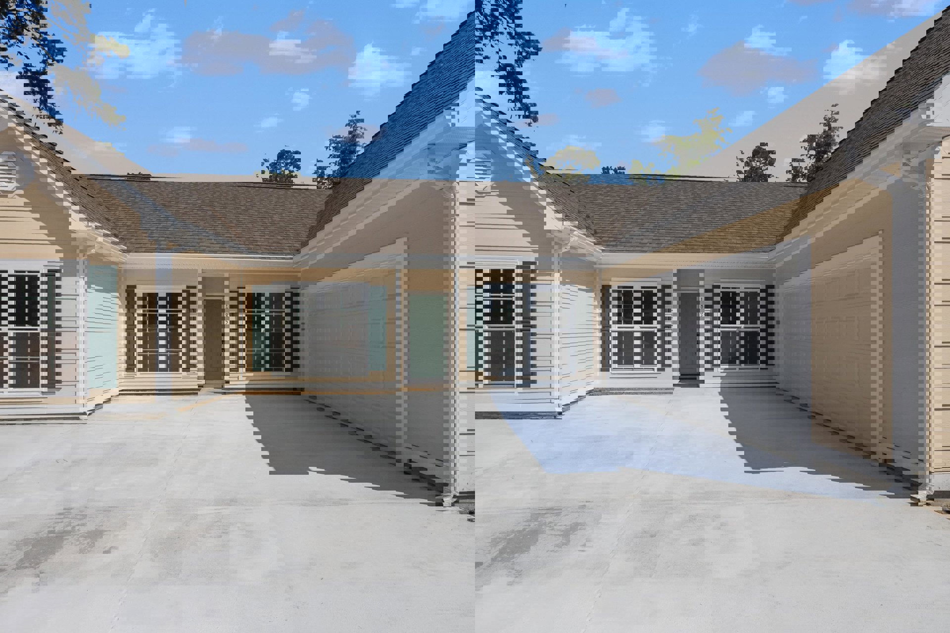 Two-story home with white siding, green front door, glass-paned windows, attached garage with concrete driveway, under blue sky with scattered clouds