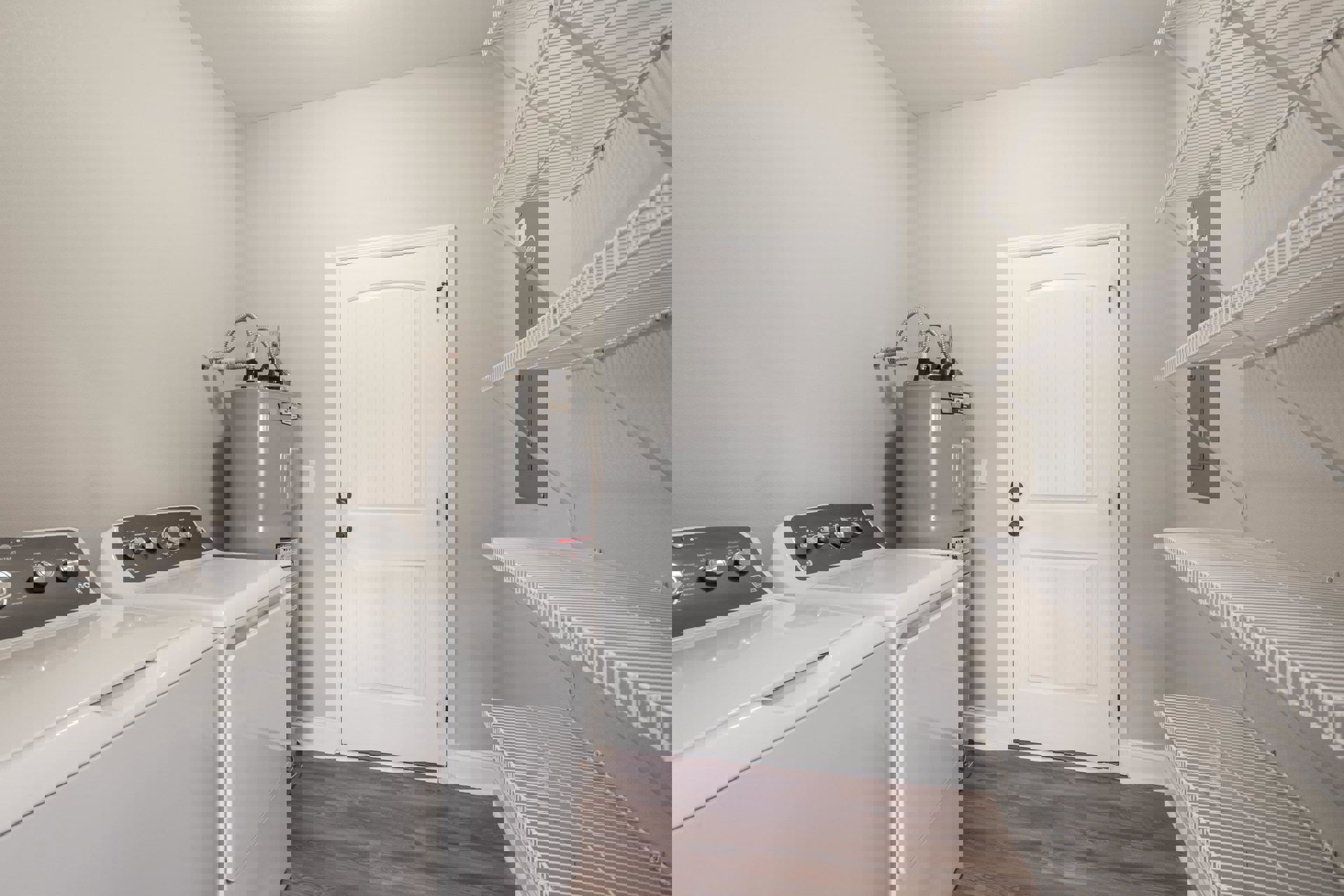 Laundry room with white tile floor, front-loading washer and dryer, white door with black knobs, white wire shelf mounted above appliances.