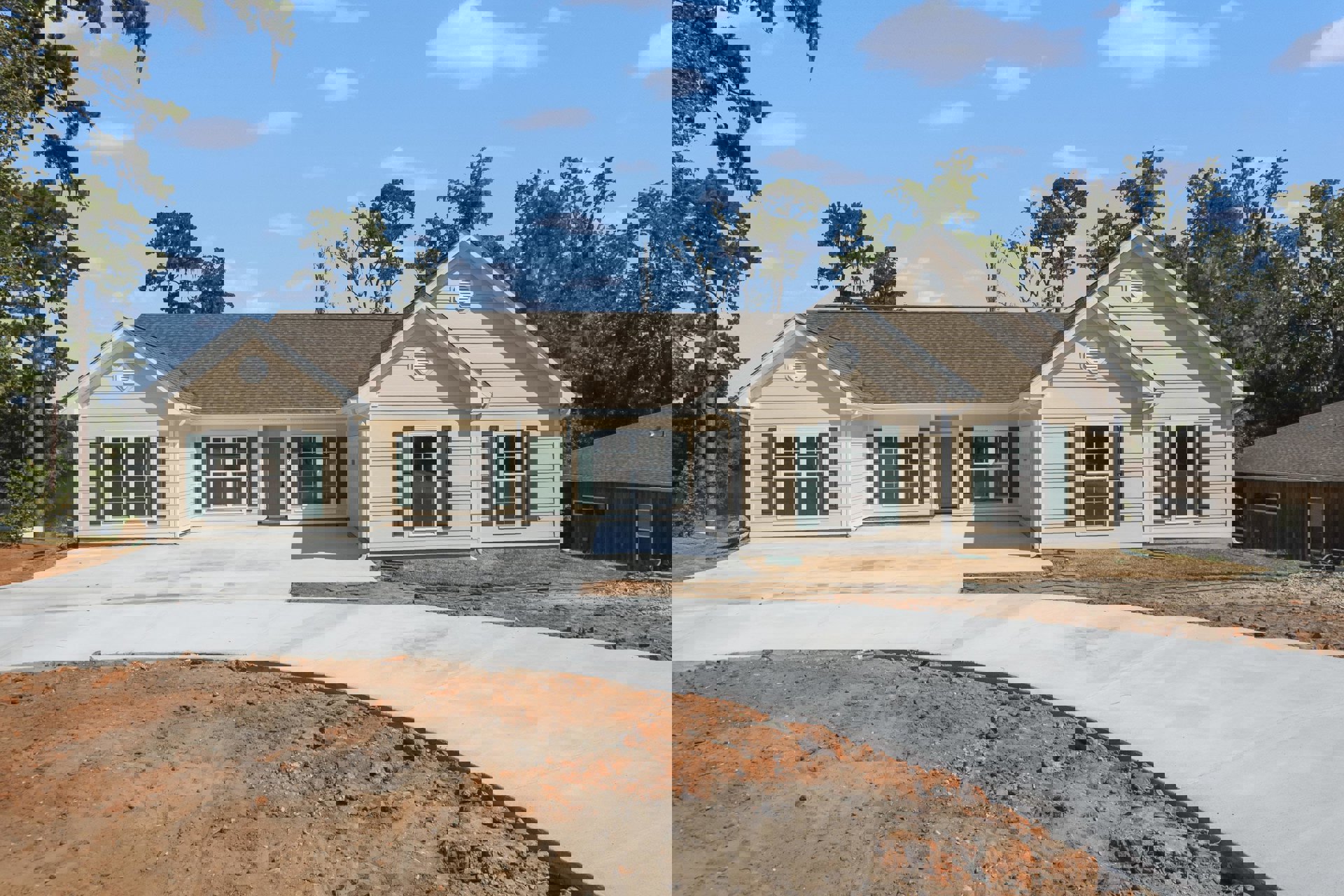 Two-story home with light siding, green shutters, attached garage with green door, paved driveway, covered front porch, mature tree, and cloudy sky