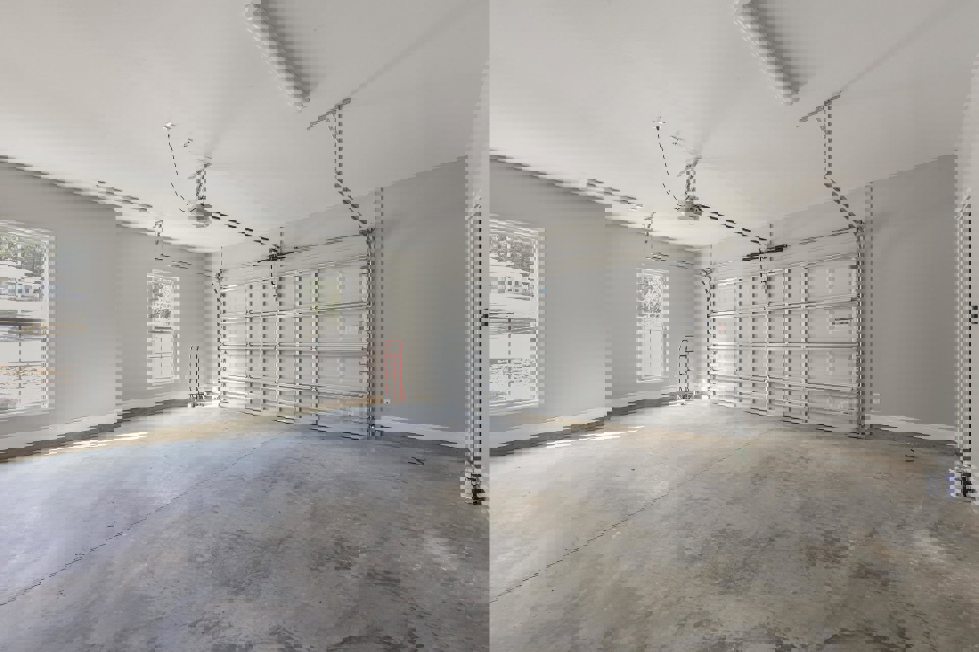 Garage interior with white plaster walls, red ladder leaning against the wall, metal garage door, exposed ceiling, concrete floor, and window overlooking green trees.