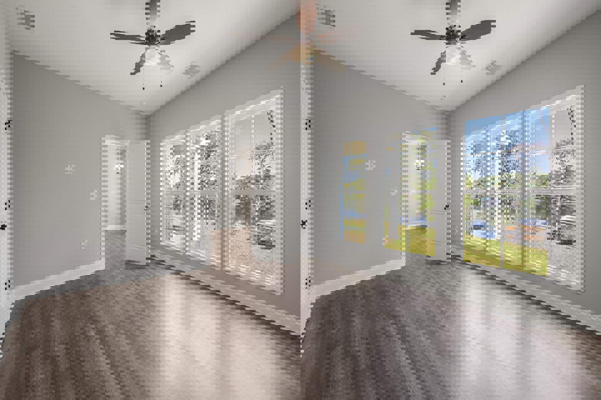 Ceiling fan with light fixture, white walls, laminate wood flooring, open white door with black knob, large window overlooking lake and trees