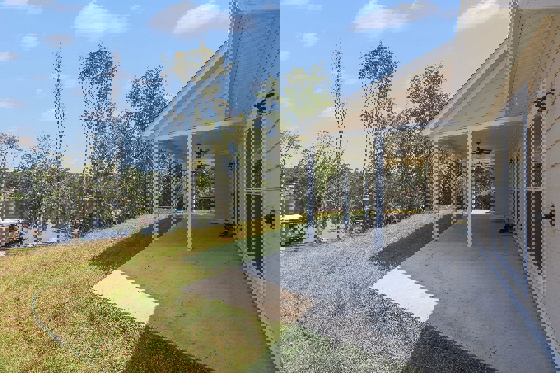 Two-story home with white covered porch, manicured lawn, mature trees, and blue sky in wooded setting