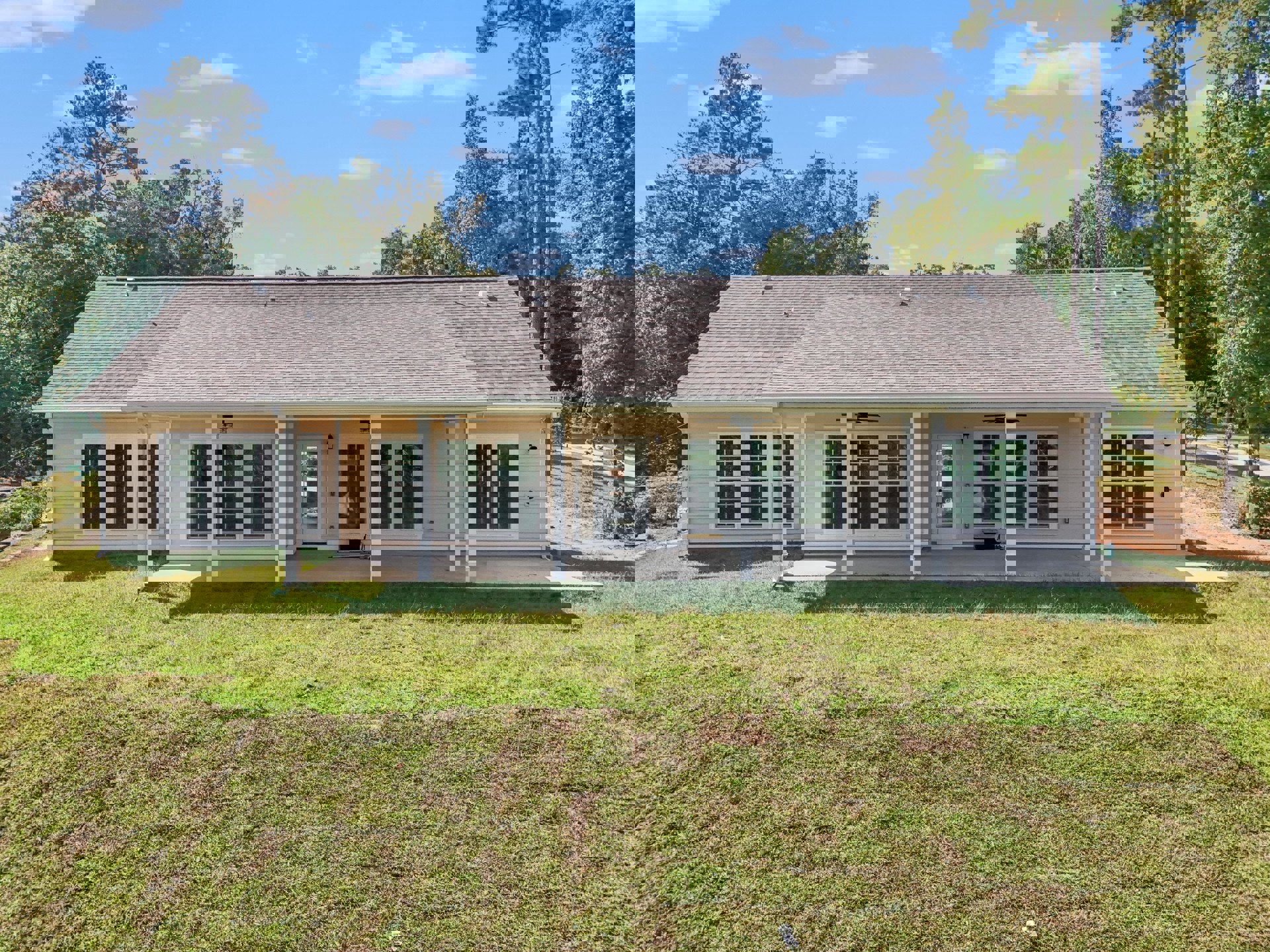 Two-story house with white siding, covered front porch, dark front door, large windows, manicured green lawn, mature trees, and blue sky with scattered clouds
