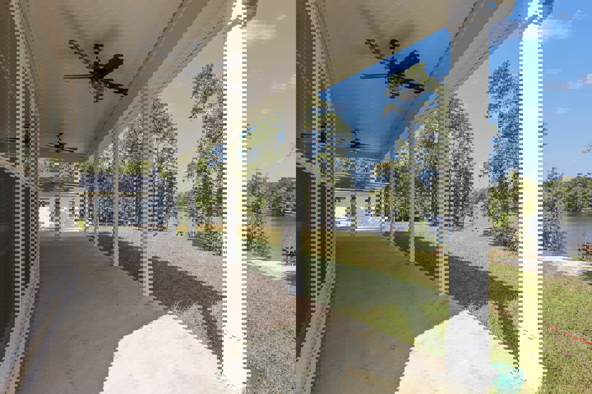 Covered porch with white pillars, ceiling fan with light, grassy lawn, and mature trees in background