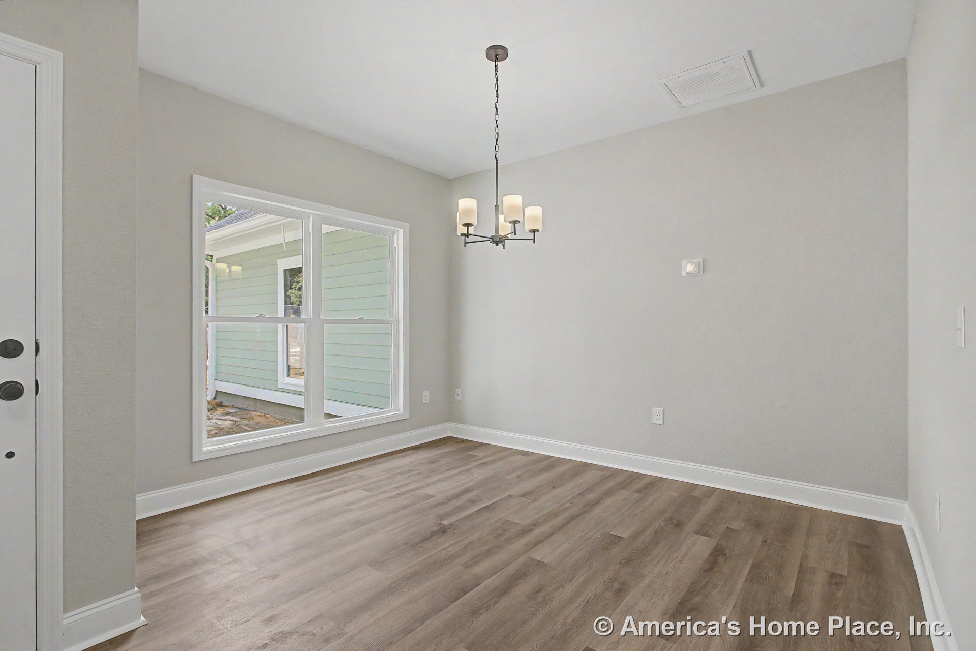 Dining area with large double window, wood-look plank flooring, modern ceiling chandelier, white baseboards, light gray walls, and ceiling vent.