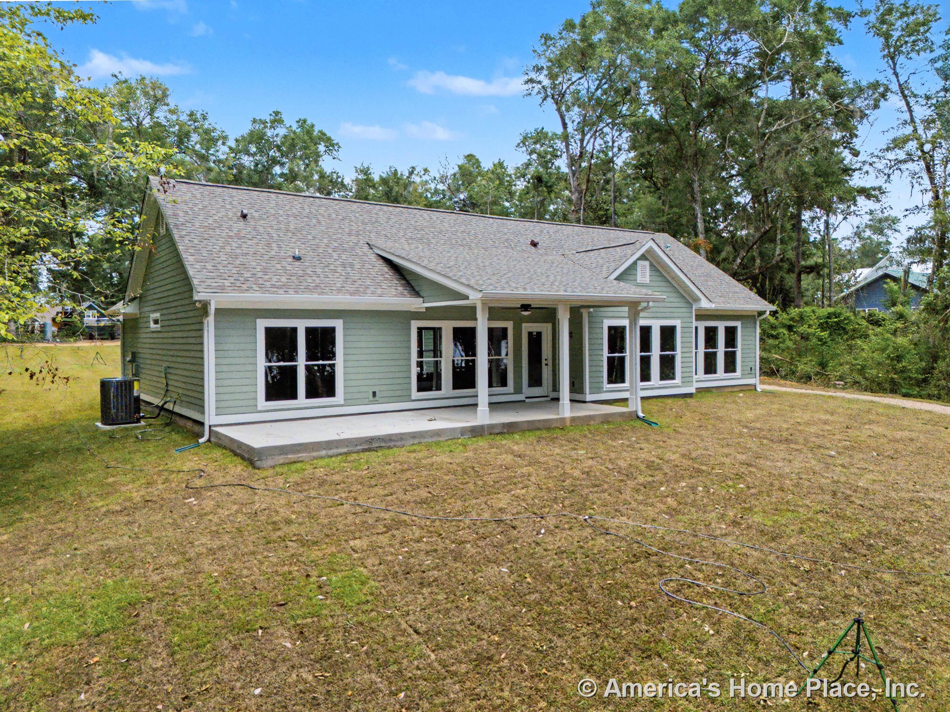 Covered rear porch with concrete patio, multiple large windows, light green siding, white trim, and gable roof.