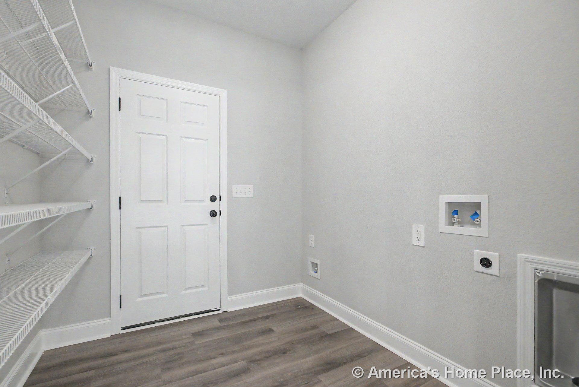 Laundry room with wall-mounted wire shelving, utility hookups, white paneled door, gray painted walls, vinyl plank flooring, and white baseboard trim.