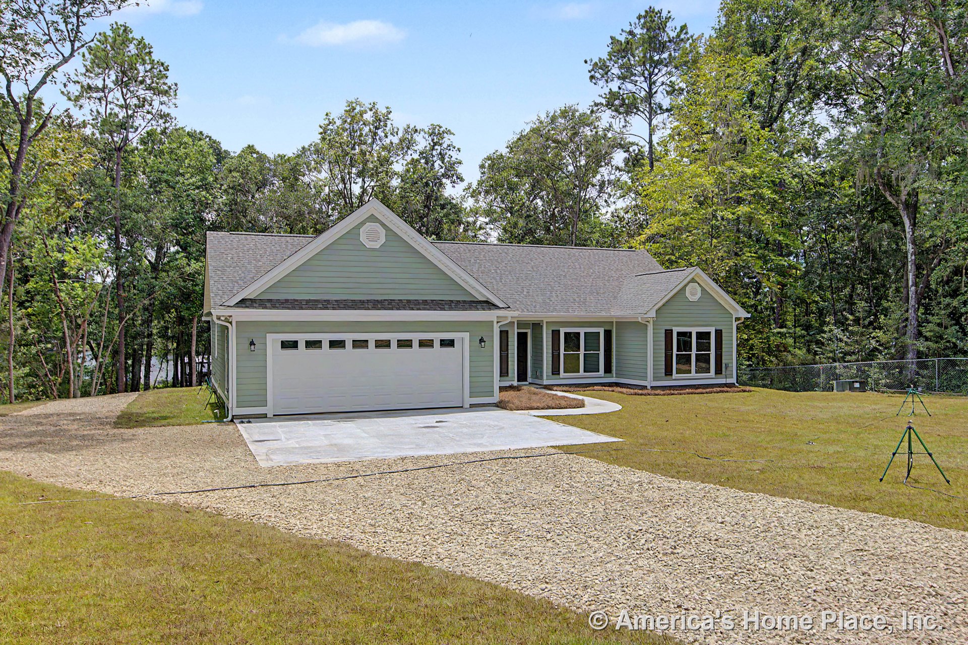 Light green horizontal siding with white trim, gable shingle roof, covered front porch, attached two-car garage with white door, multiple large windows, paved driveway