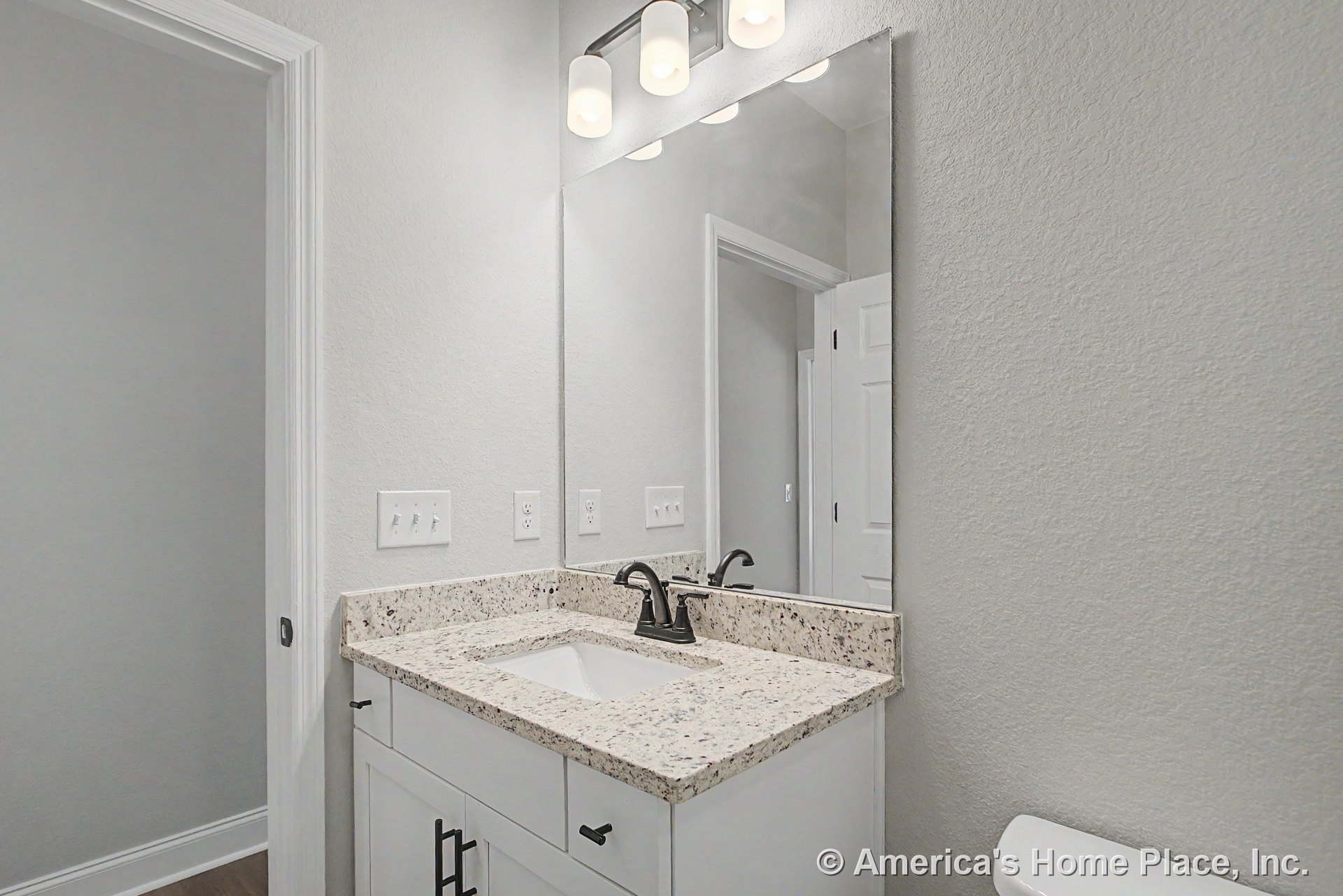Granite countertop vanity with white shaker cabinetry, undermount sink, matte black faucet, wall-mounted mirror, and three-light vanity fixture.