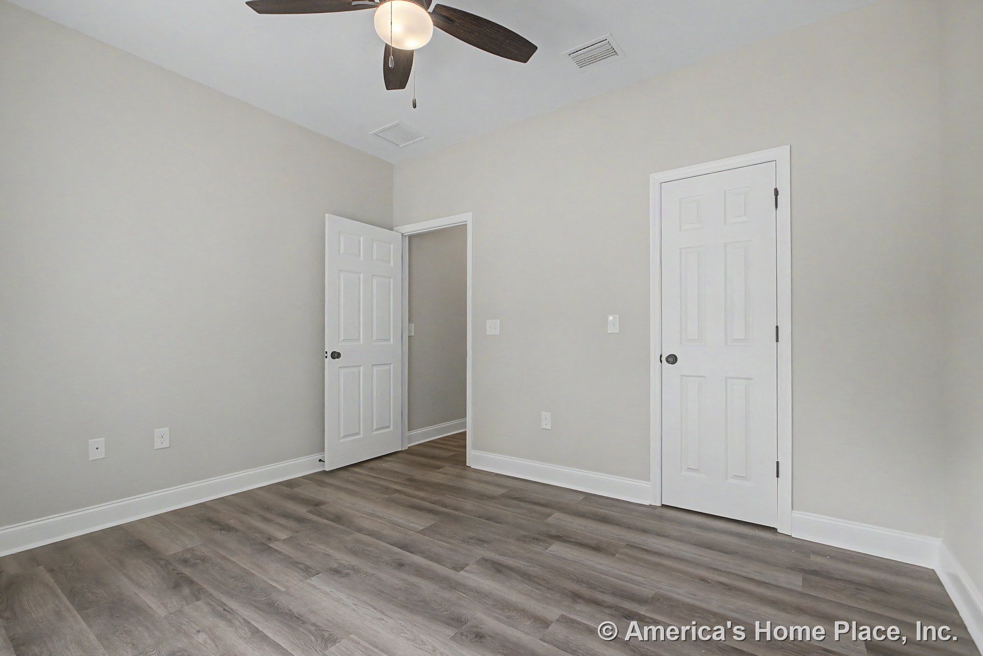 Bedroom with light gray walls, white baseboard trim, wood-look vinyl plank flooring, ceiling fan with integrated light, recessed ceiling vent, and white paneled closet and entry