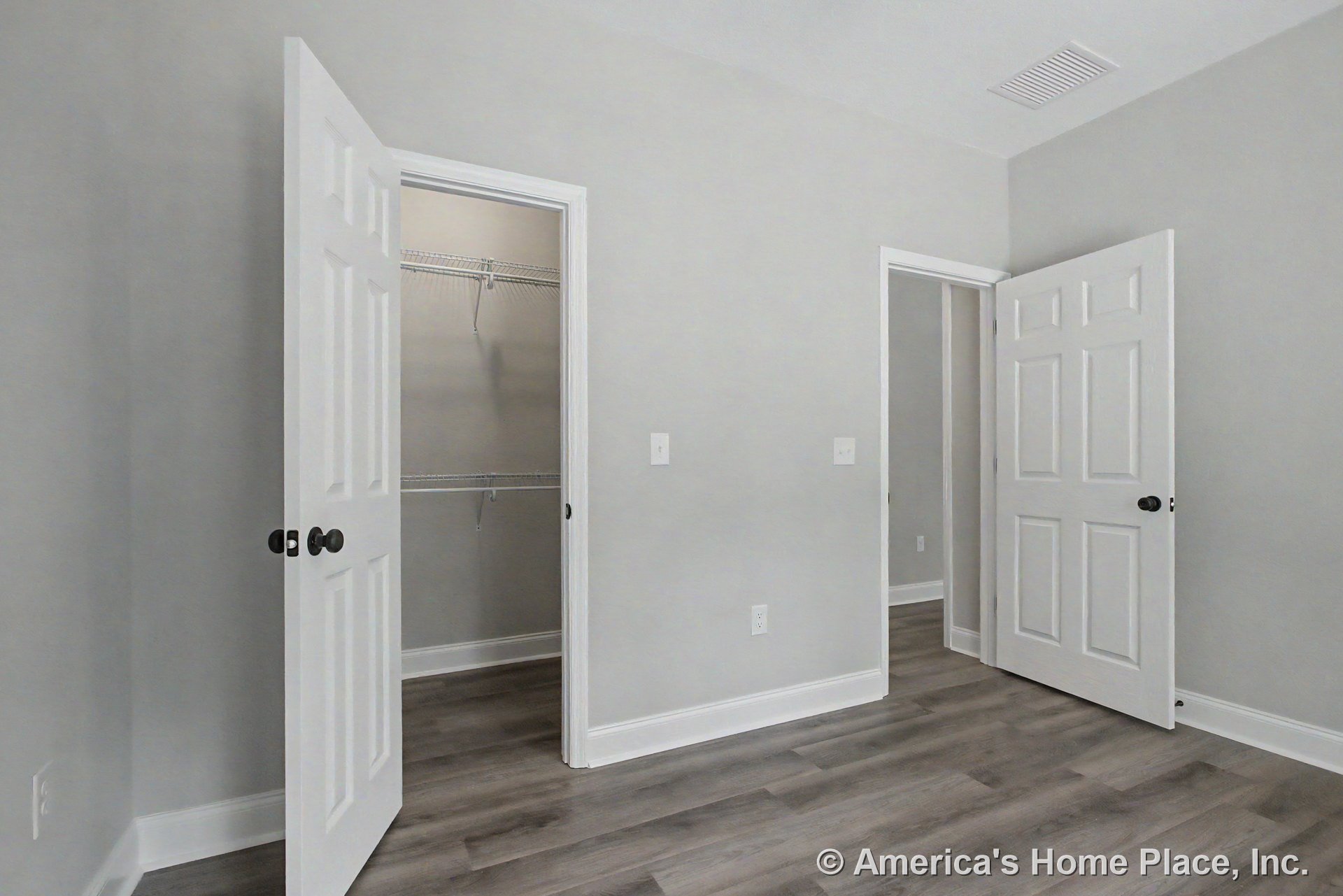 Bedroom with white paneled closet door, walk-in closet featuring wire shelving, gray wood-look flooring, light gray painted walls, white baseboards and trim, and ceiling vent.