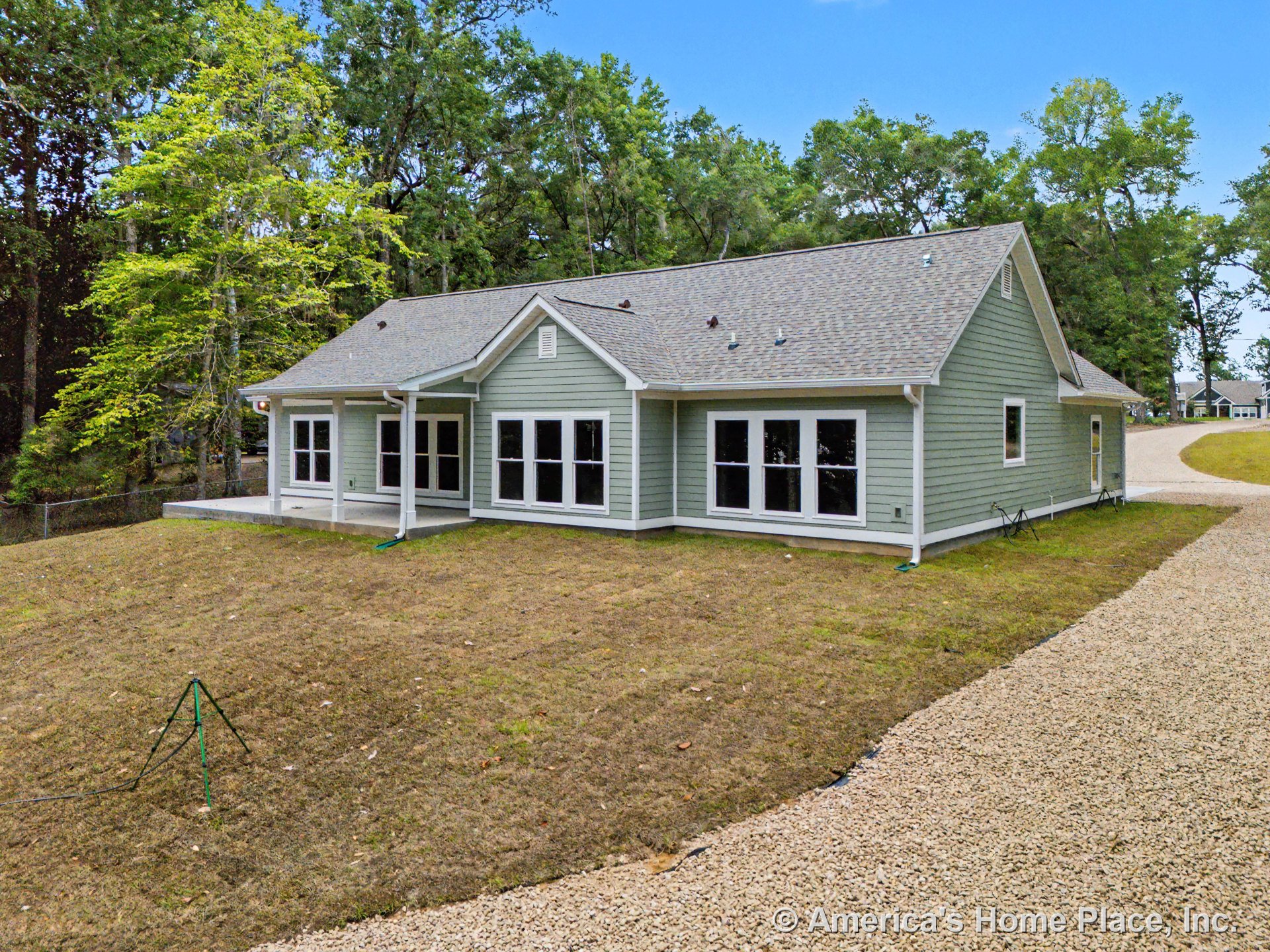 Covered rear porch with gray lap siding, white trim, multiple large windows, asphalt shingle roof, and gravel driveway on single-story home exterior.