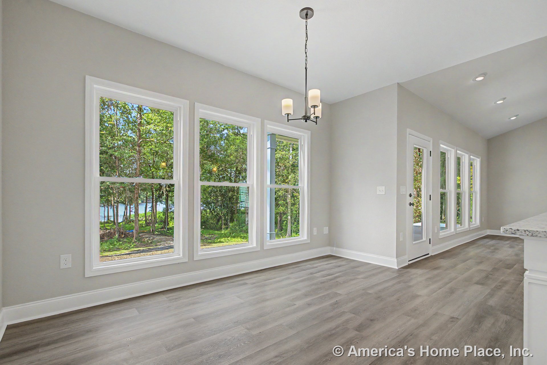Dining area with three-pane windows, modern pendant light fixture, light gray walls, white baseboards, wood-look vinyl plank flooring, glass exterior door, and open layout with
