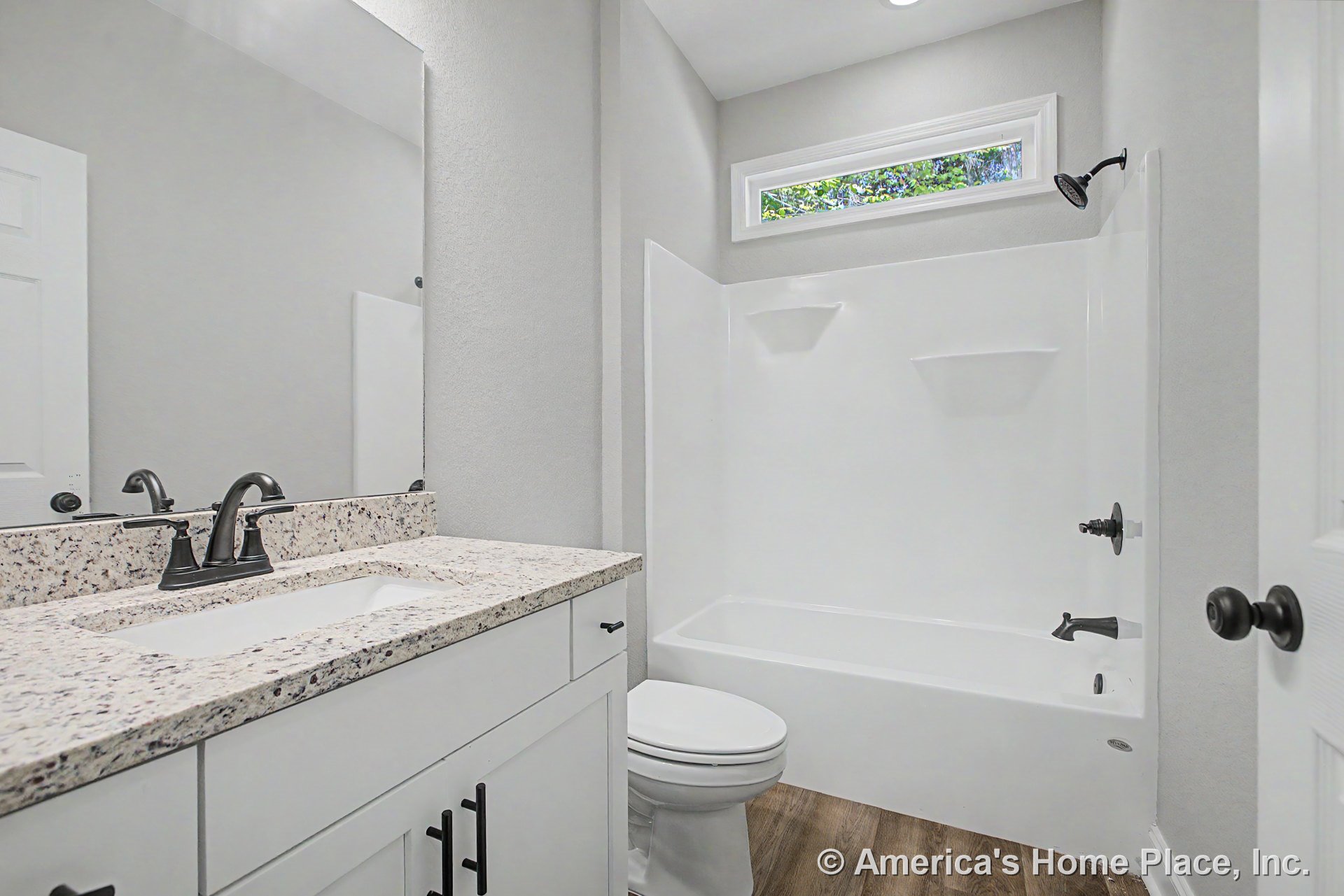 White shaker vanity with granite countertop, built-in bathtub and shower, horizontal window above tub, wood-look flooring, matte black fixtures, framed mirror, recessed lighting