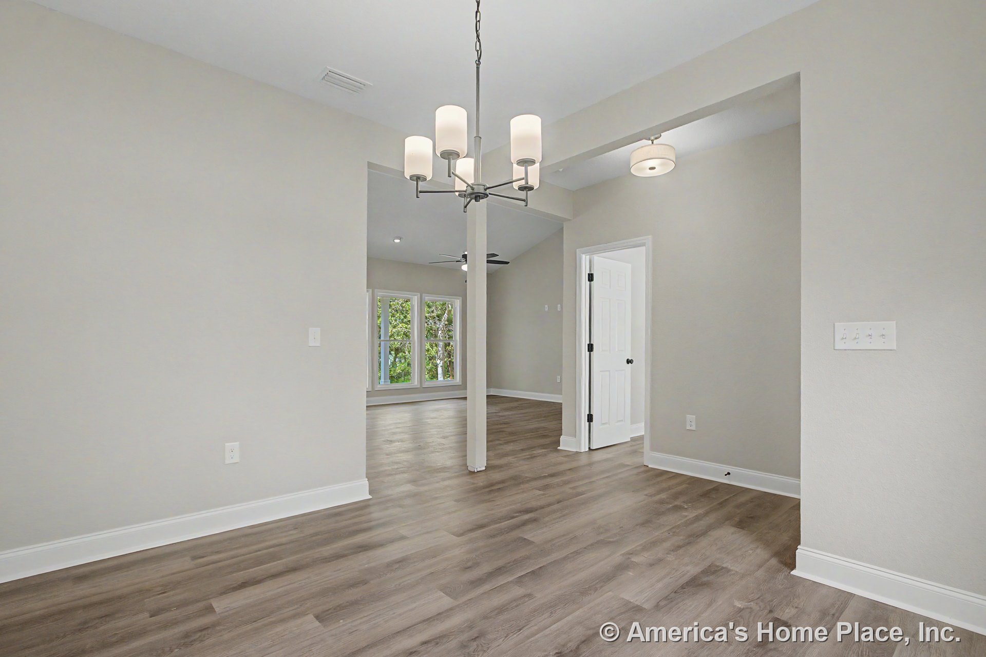 Modern dining area with contemporary chandelier, wide plank vinyl flooring, white baseboards, neutral walls, open doorway leading to living room, large windows, and flush mount