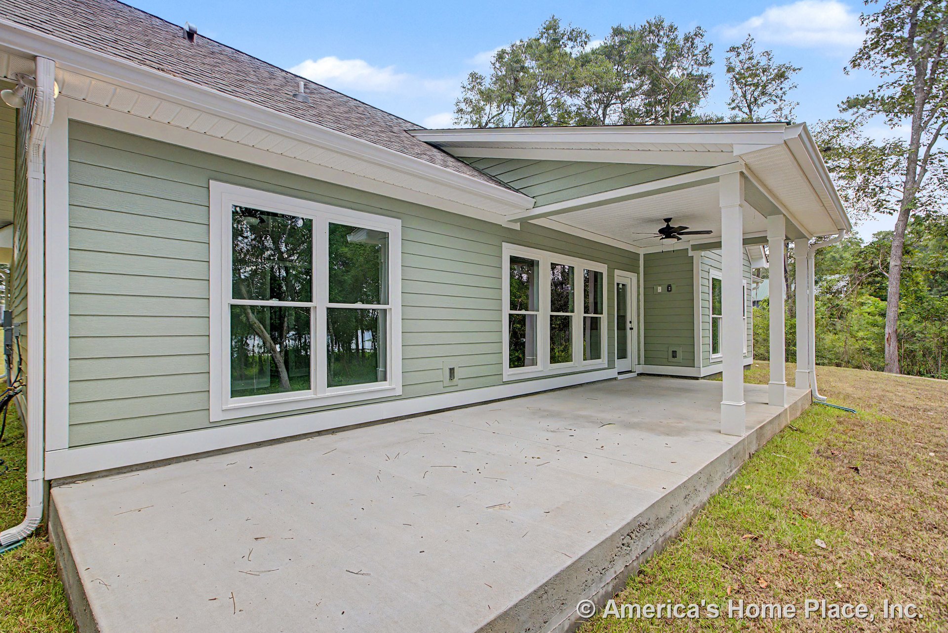 Covered back porch with concrete slab flooring, multiple large windows with white trim, ceiling fan fixture, exterior door, and supporting columns beneath siding.