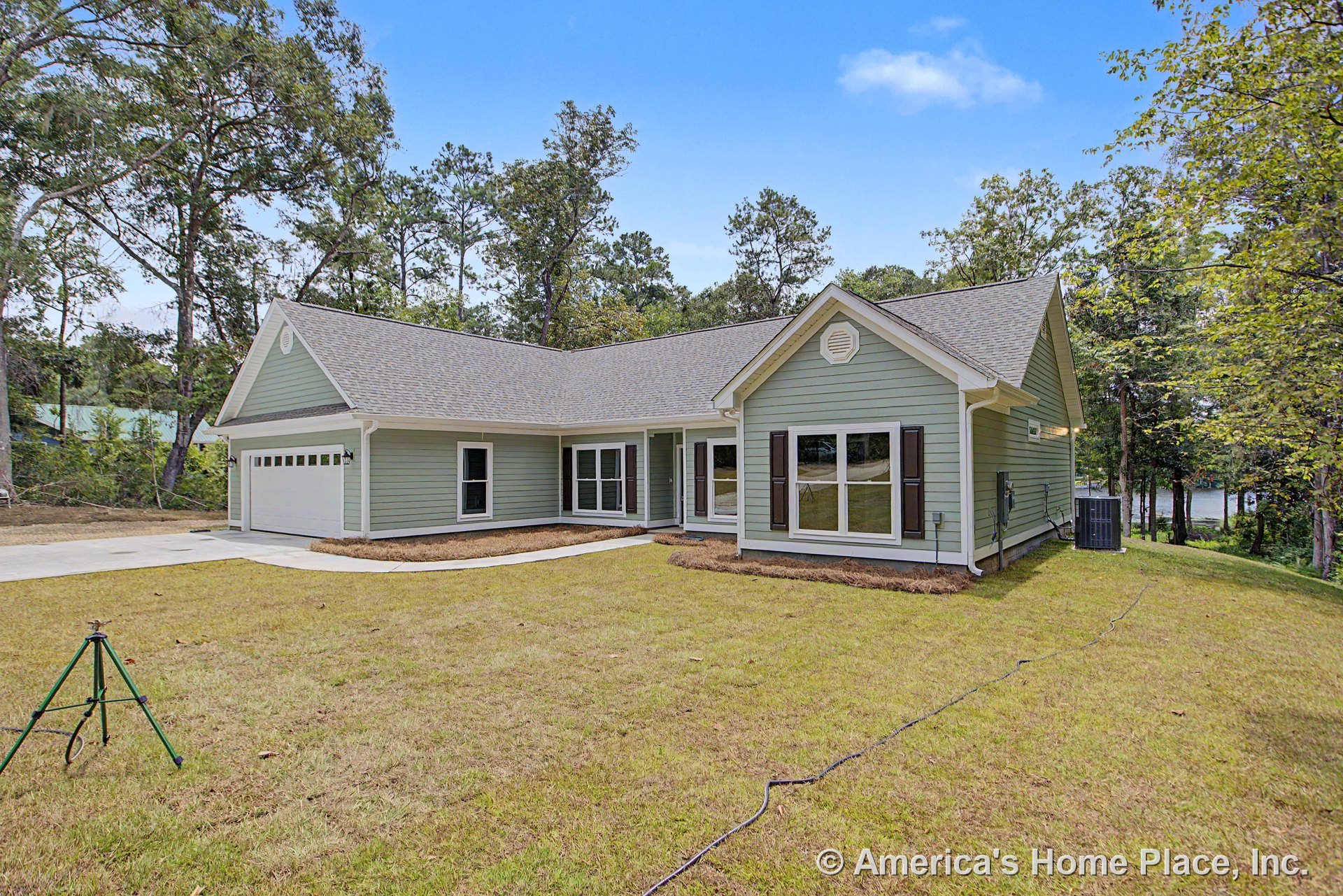 Light green horizontal siding with white trim and gutters, gable roof featuring vented detail, large double-hung windows with exterior shutters, attached two-car garage, covered