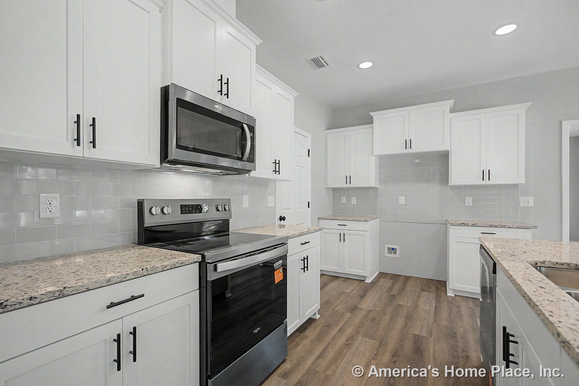 White shaker cabinets with granite countertops, stainless steel oven and microwave, subway tile backsplash, recessed ceiling lights, and wood-look flooring.
