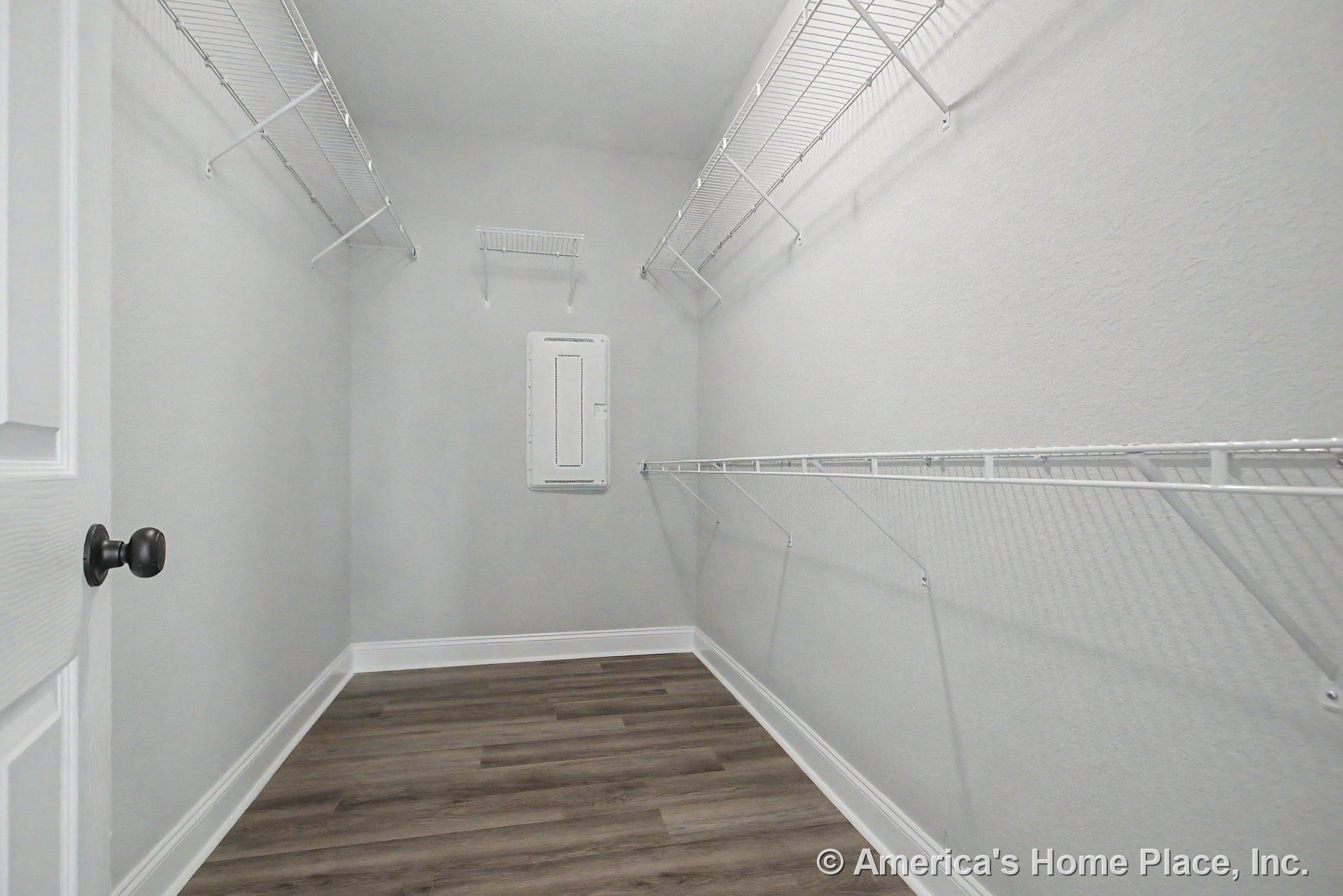 Walk-in closet with multiple white wire shelving units, wood-look vinyl flooring, gray painted walls, white baseboards, and visible utility panel.