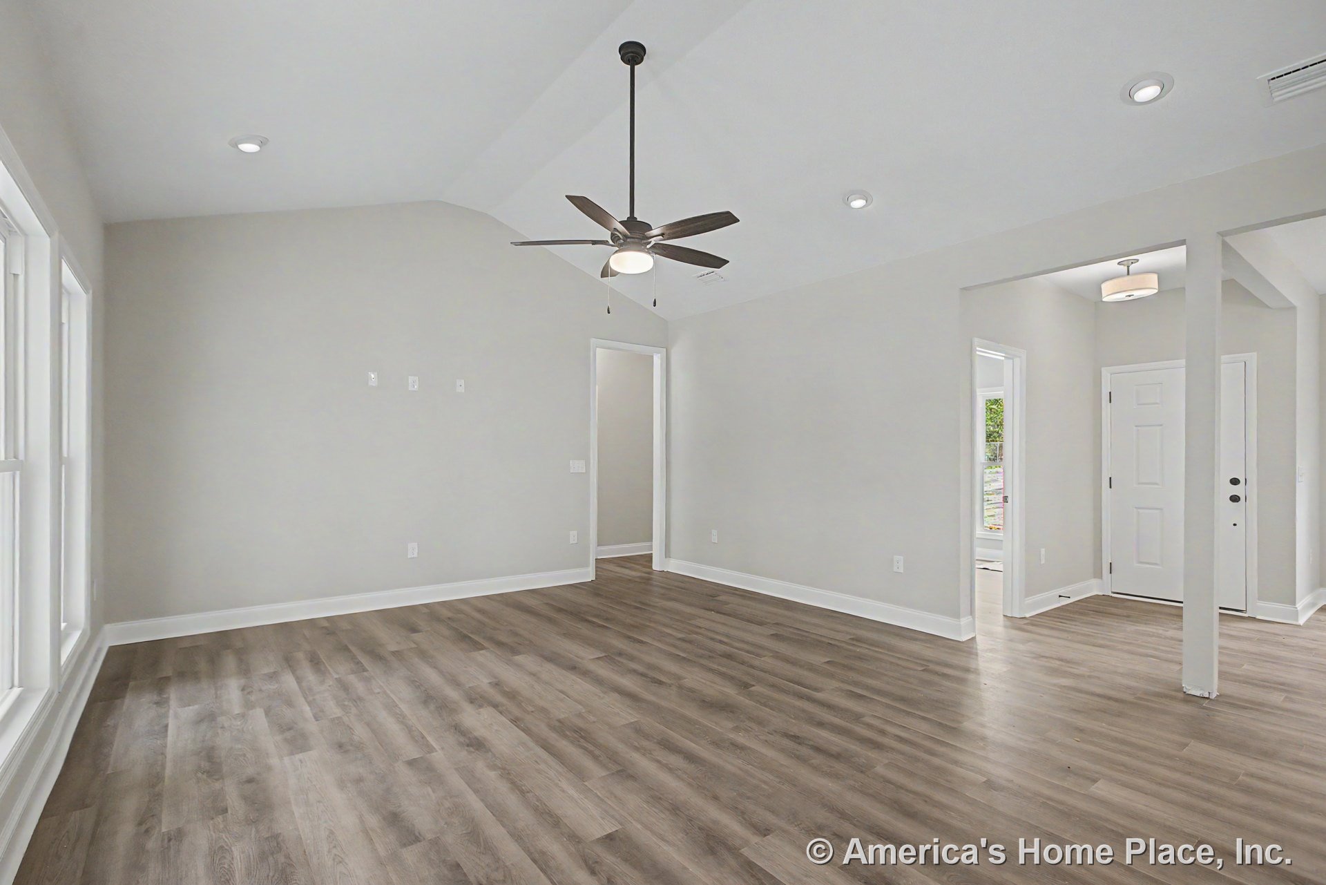 Vaulted ceiling with recessed lighting and ceiling fan, expansive window wall, wood-look flooring, white trim and baseboards, neutral walls, entry door, open layout.