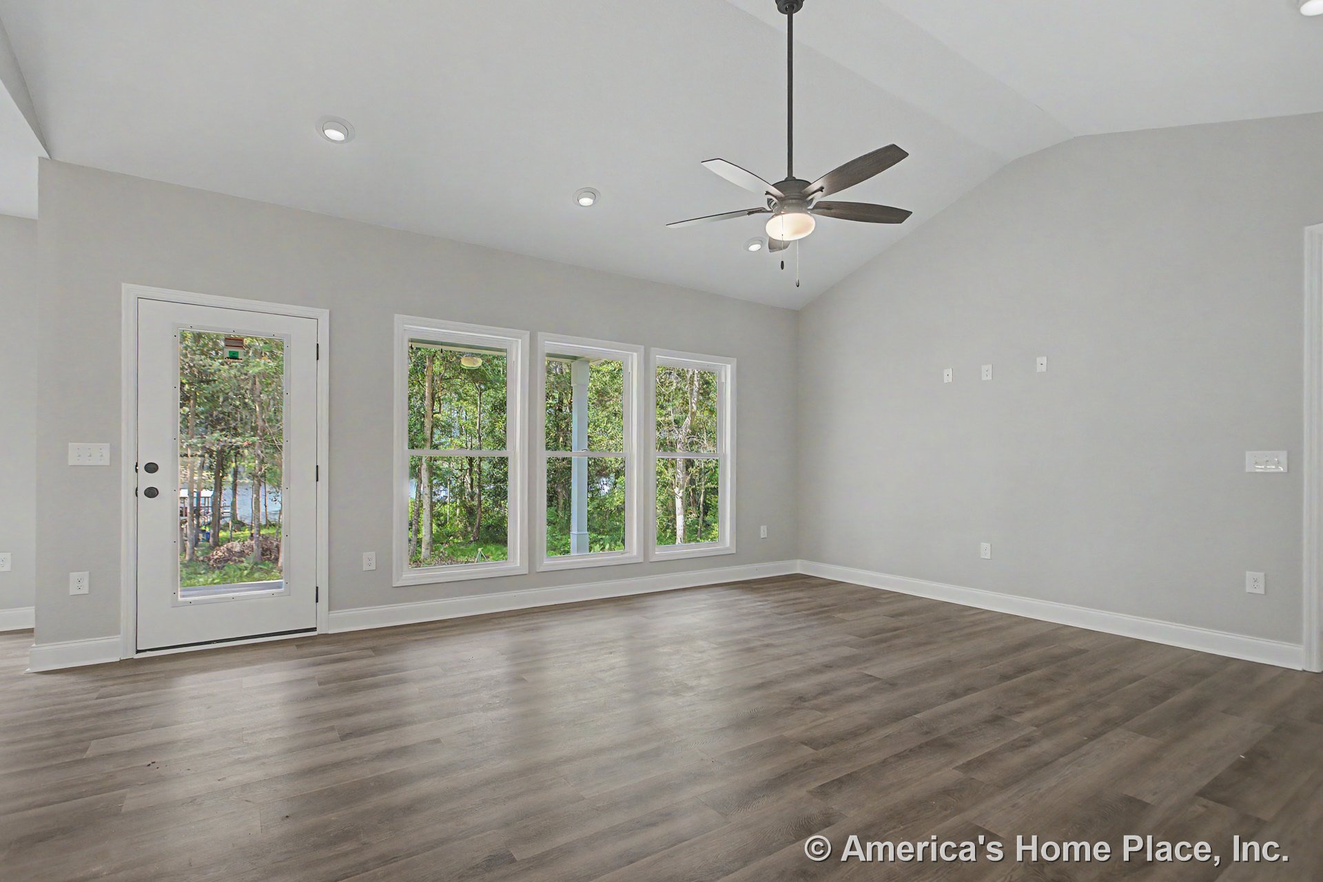 Vaulted living room ceiling with recessed lighting and modern ceiling fan, three-panel picture windows and glass exterior door with white trim, wide plank wood-look flooring