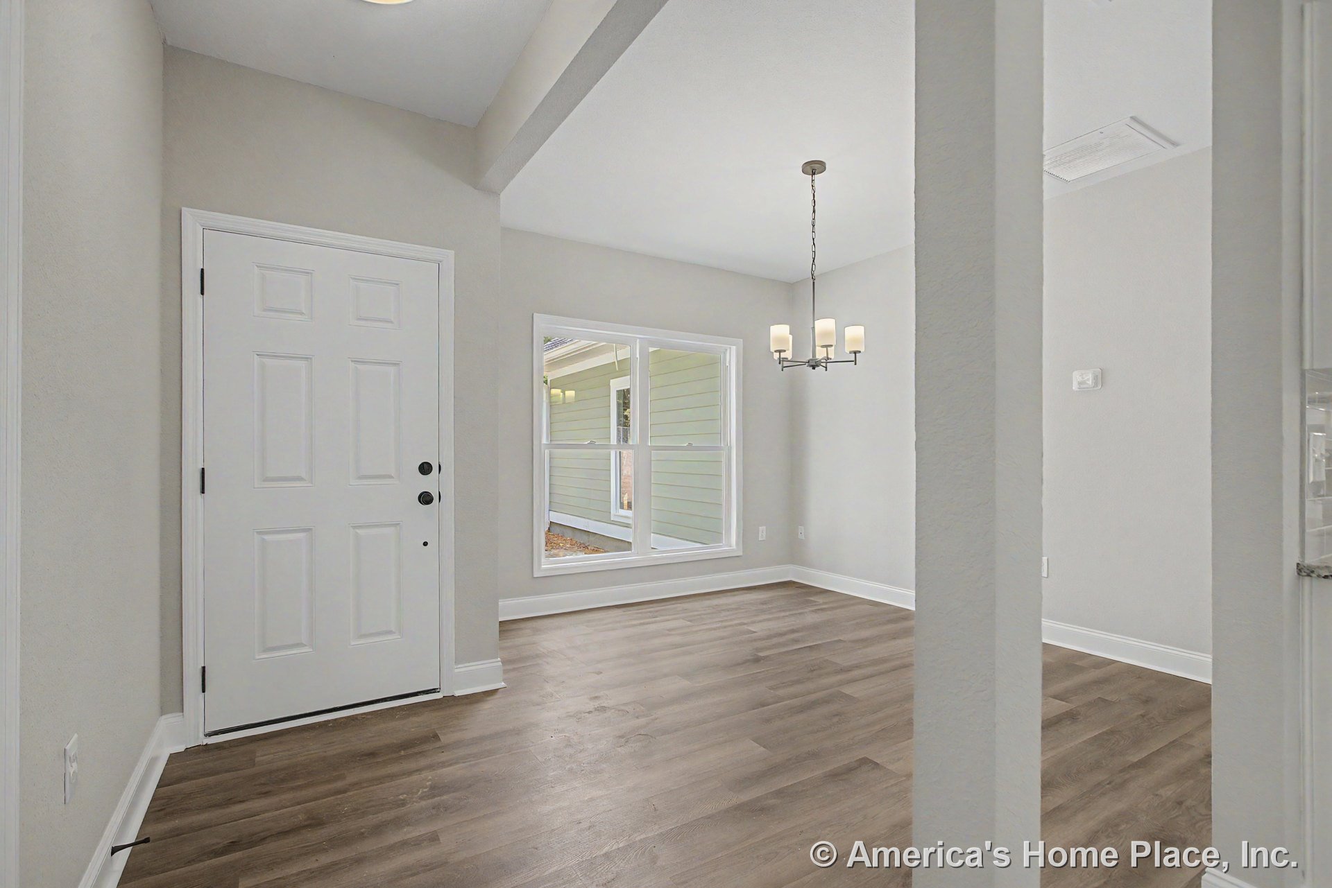 White paneled front door with adjacent large double window, wood-look plank flooring, modern chandelier lighting, light gray painted walls, and white baseboard trim in a bright